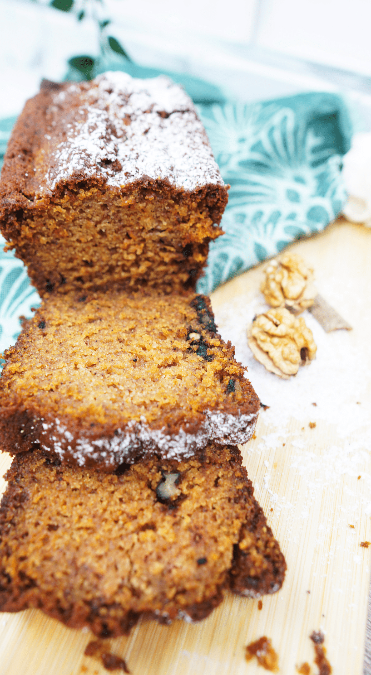 Close-up of sliced pumpkin bread loaf dusted with powdered sugar on a wooden board.