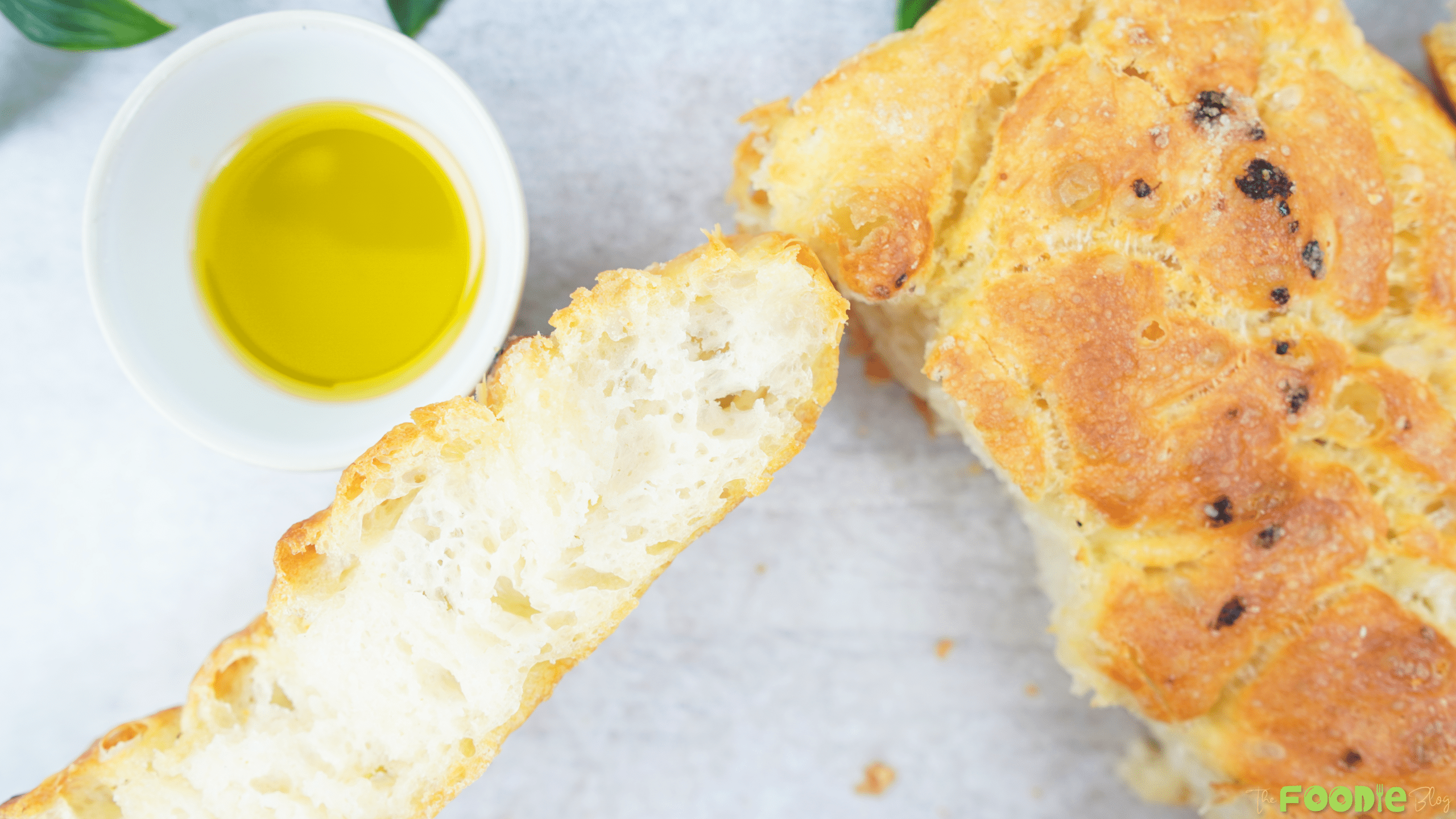 Golden focaccia-style bread with a torn piece and a small bowl of olive oil
