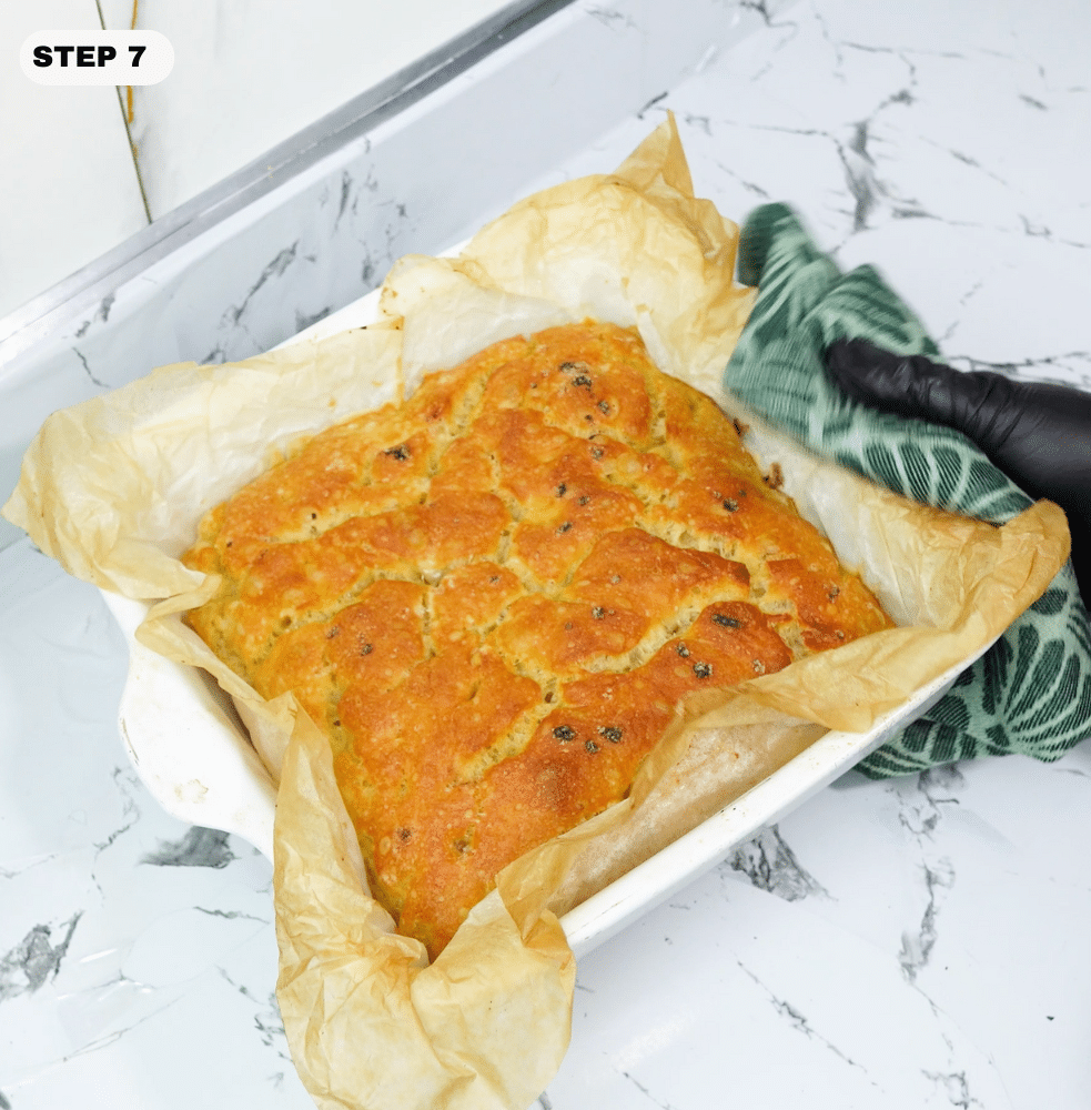 Freshly baked focaccia-style bread being lifted from the baking dish