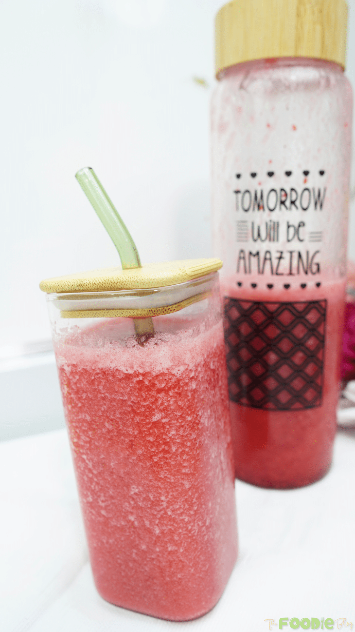 Iced raspberry juice in a square glass with a straw, with a bottle of juice in the background
