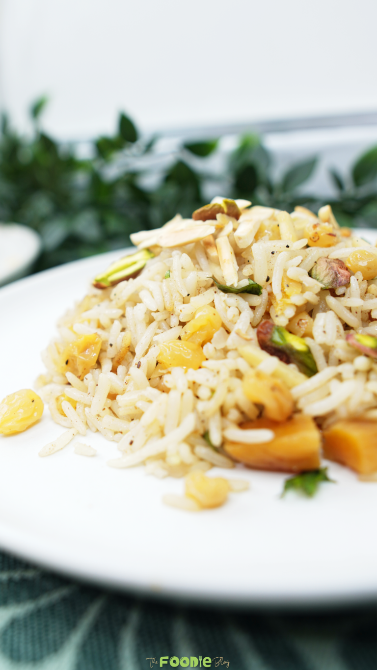 Close-up side view of rice pilaf with raisins, dried apricots, pistachios, and sliced almonds on a white plate