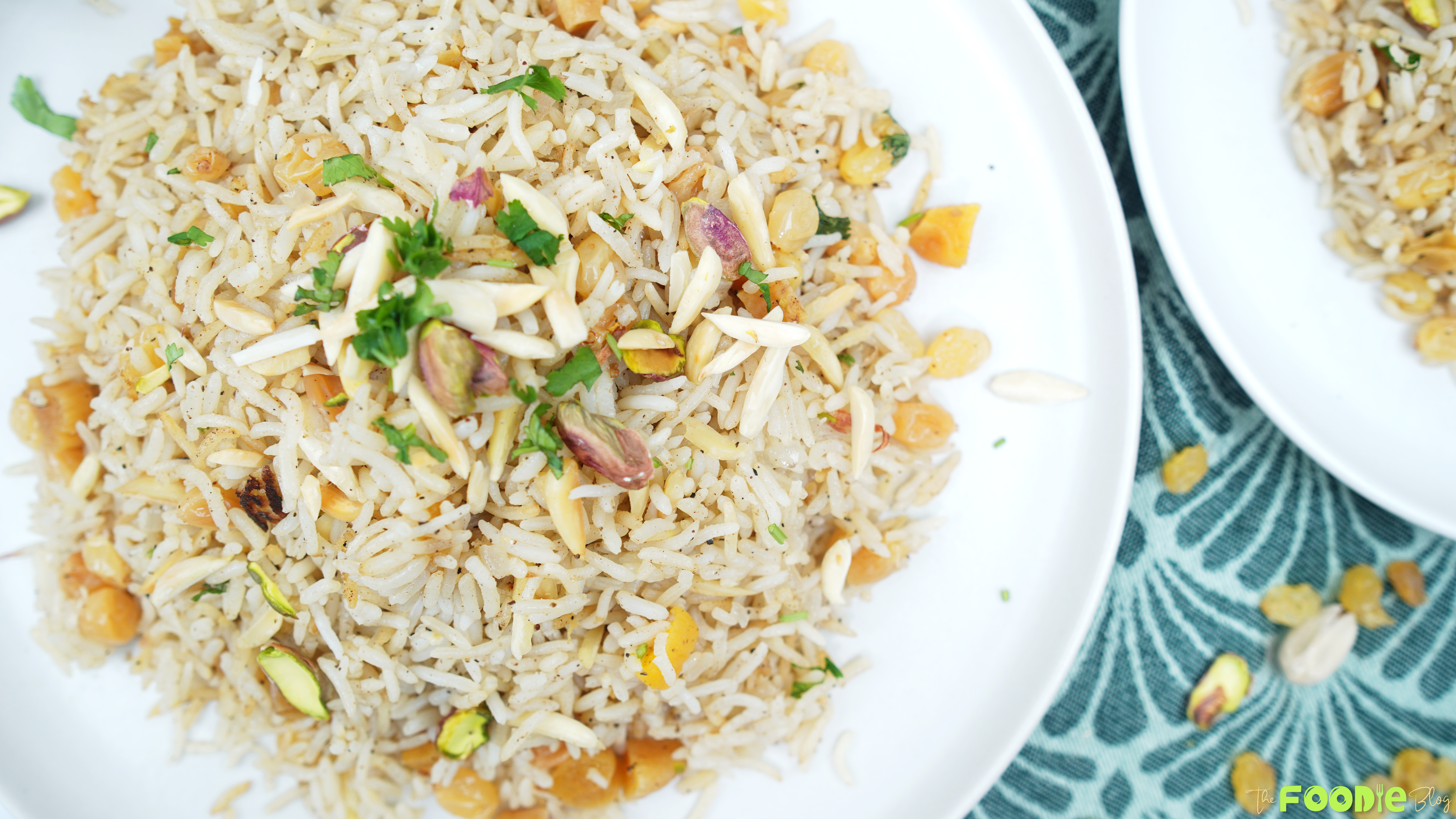 Overhead view of basmati rice pilaf topped with pistachios, slivered almonds, and parsley on a white plate