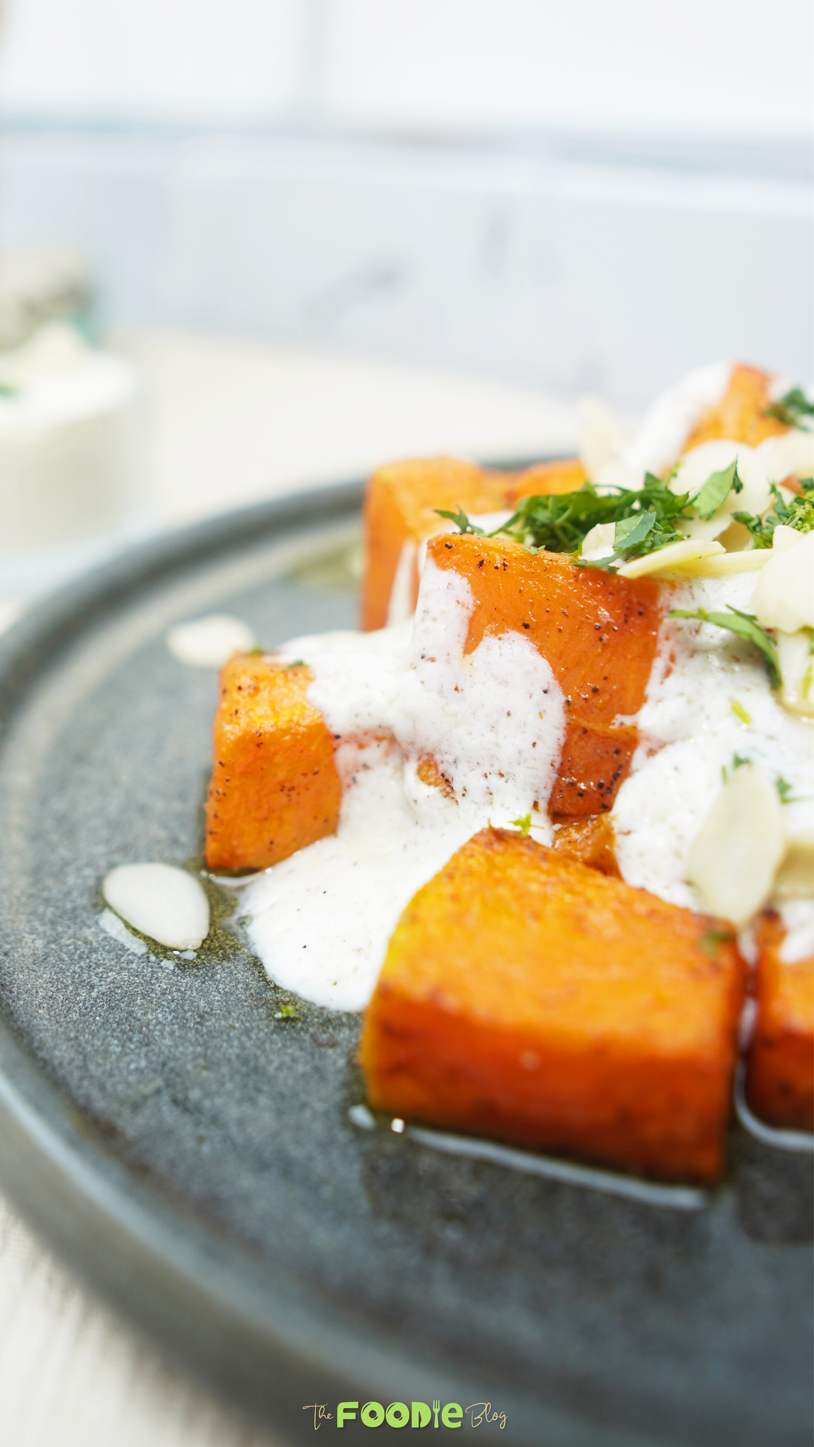 Close-up of roasted pumpkin with creamy yogurt sauce and sliced almonds on a plate
