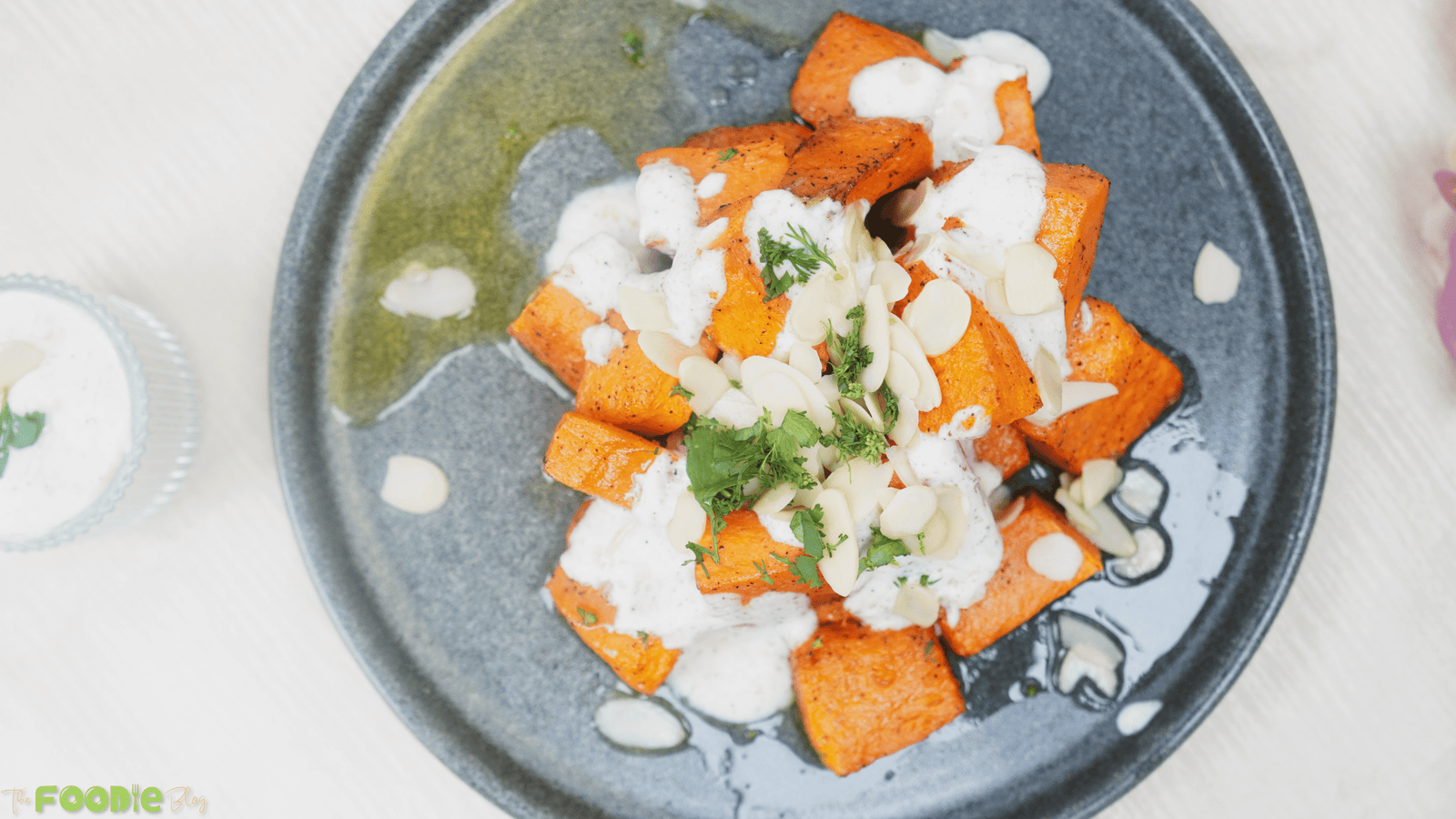 Overhead view of plated roasted pumpkin topped with yogurt sauce, herbs, and almonds
