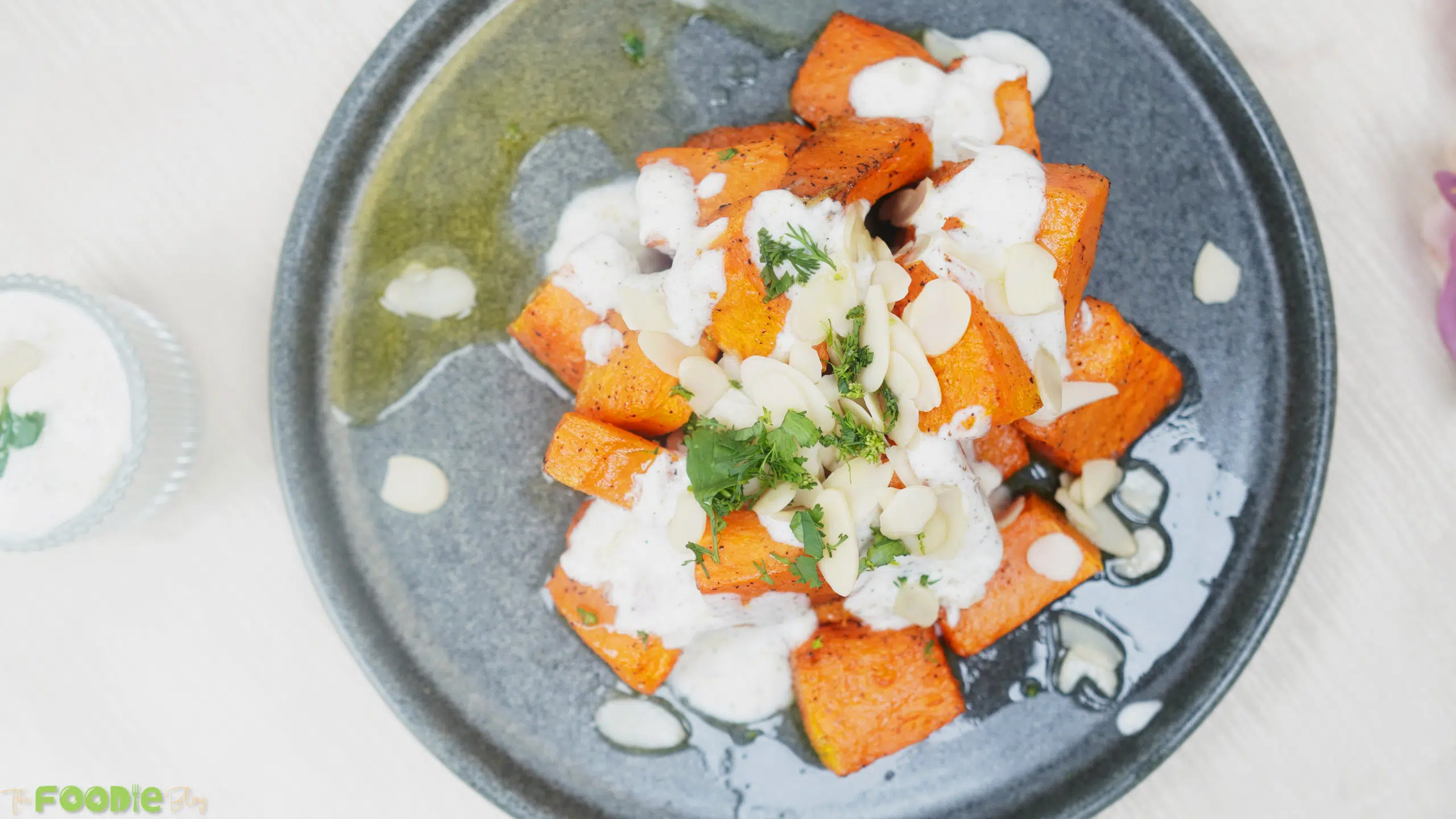 Overhead view of plated roasted pumpkin topped with yogurt sauce, herbs, and almonds