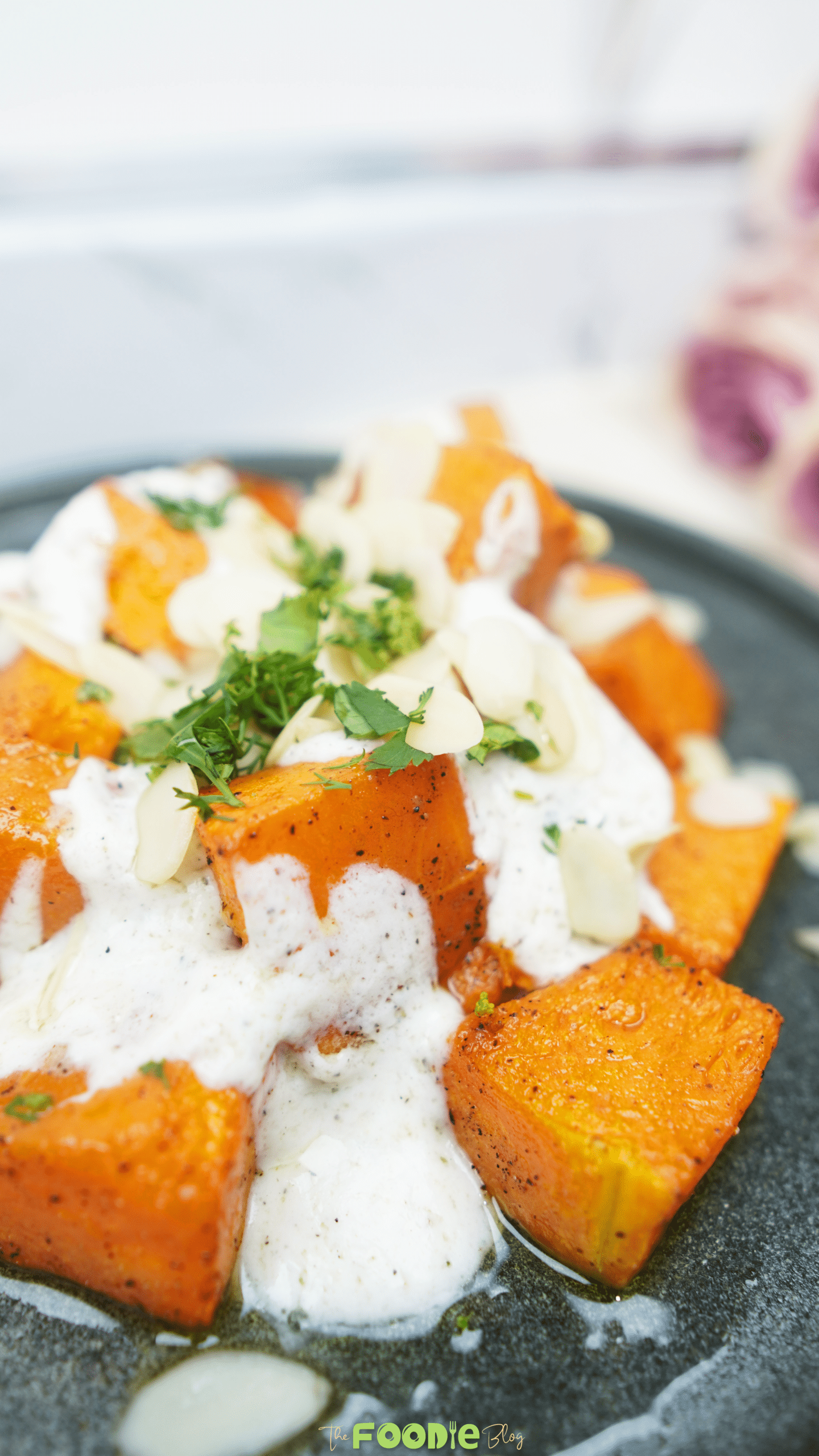 Roasted pumpkin cubes topped with lemon yogurt sauce, almonds, and parsley on a gray plate