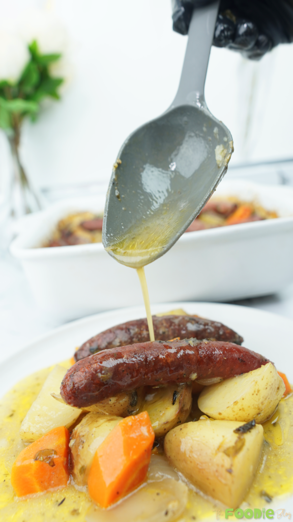 Plated sausage bake with browned sausages, potatoes, carrots, and onions topped with warm gravy.