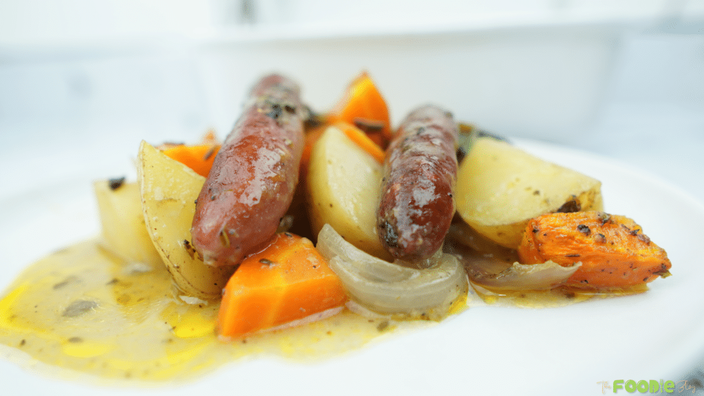 Plated sausages with baby potatoes, carrots, and onions in a light pan gravy
