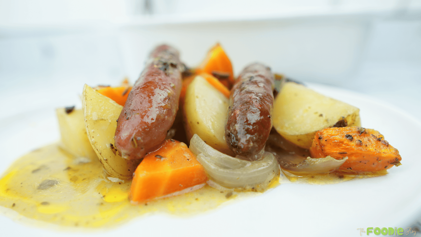 Plated sausages with baby potatoes, carrots, and onions in a light pan gravy