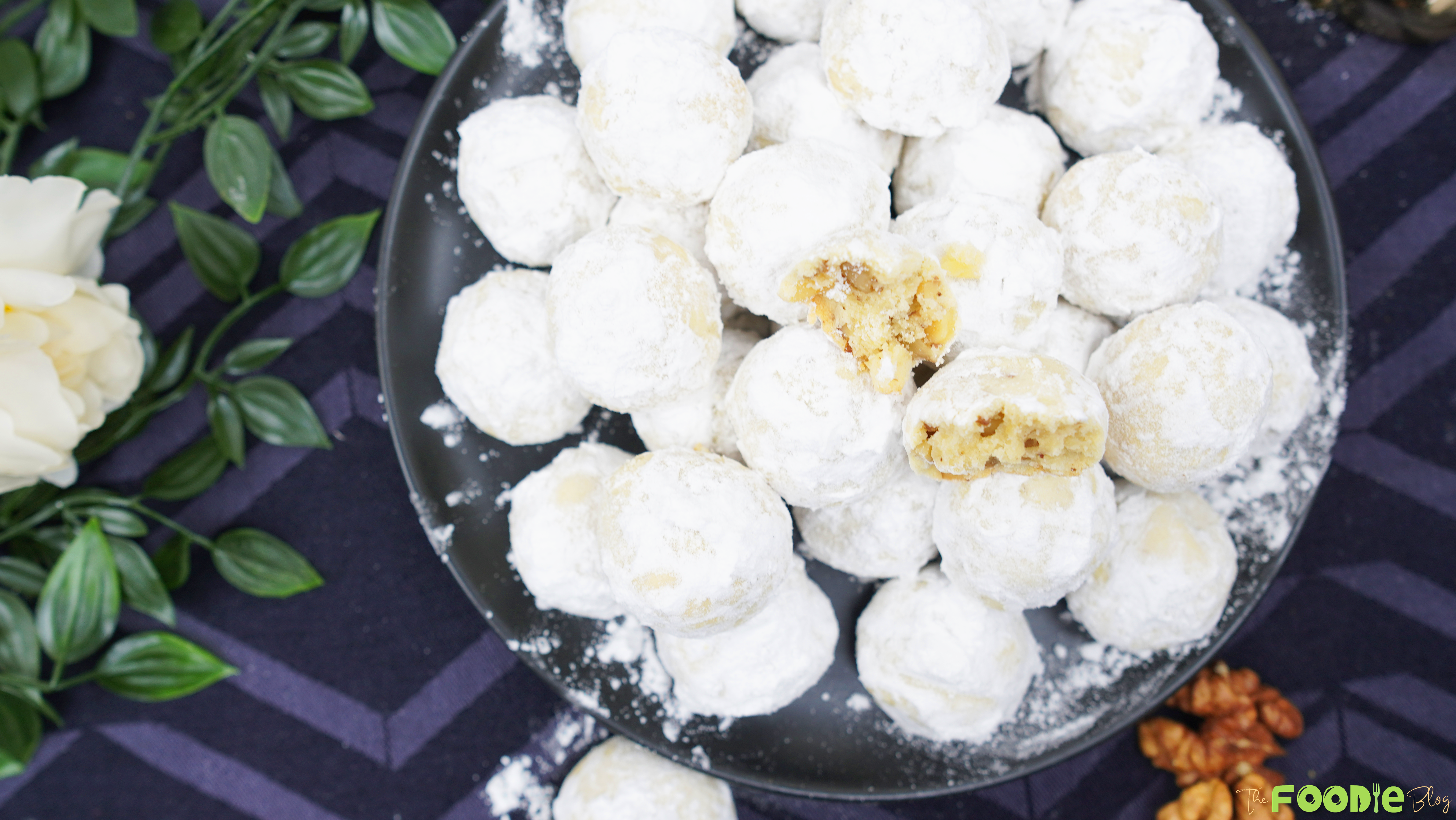 Overhead view of a plate piled with snowball cookies coated in powdered sugar with a few cookies broken open