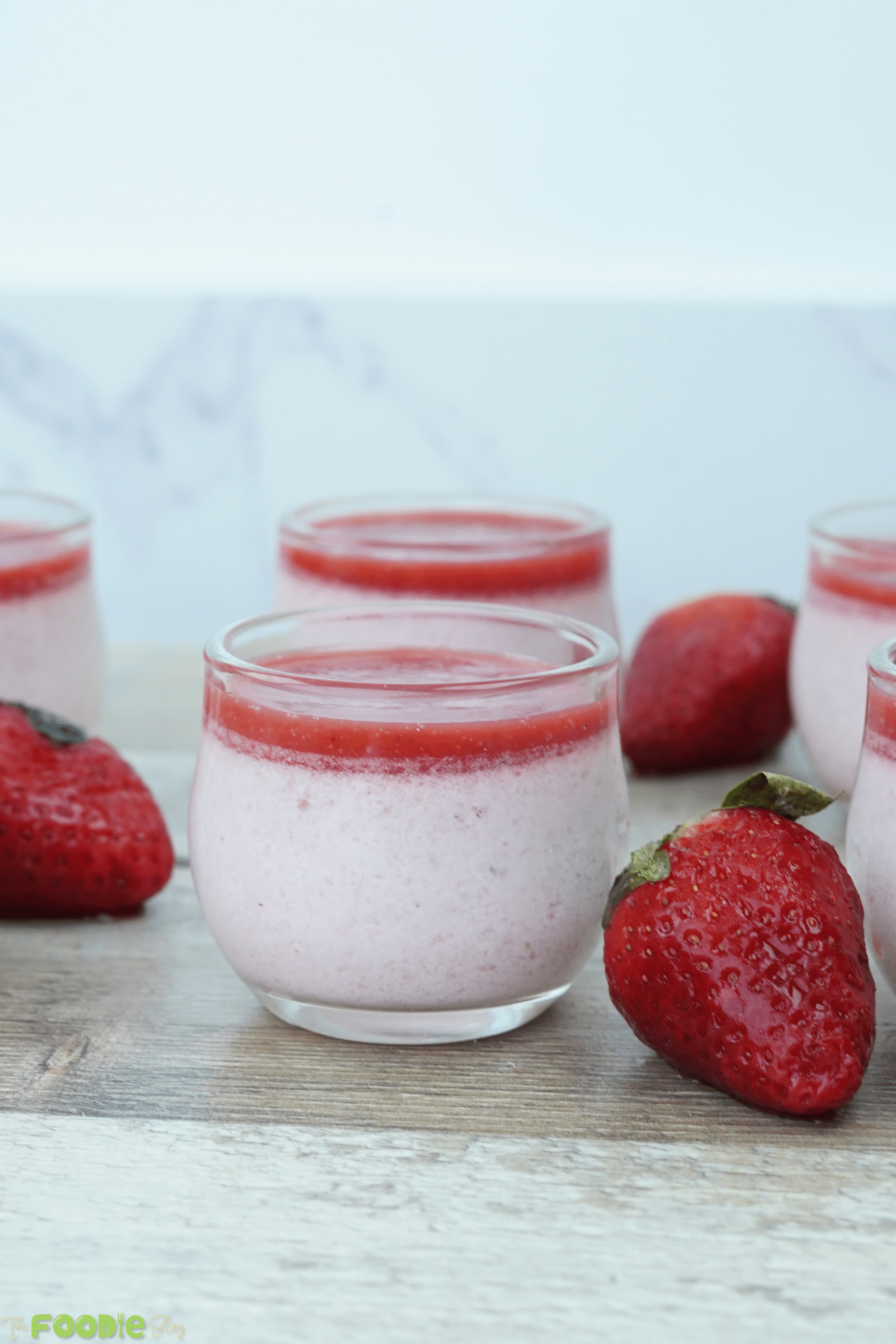 Strawberry panna cotta cups with fresh strawberries on a wooden surface