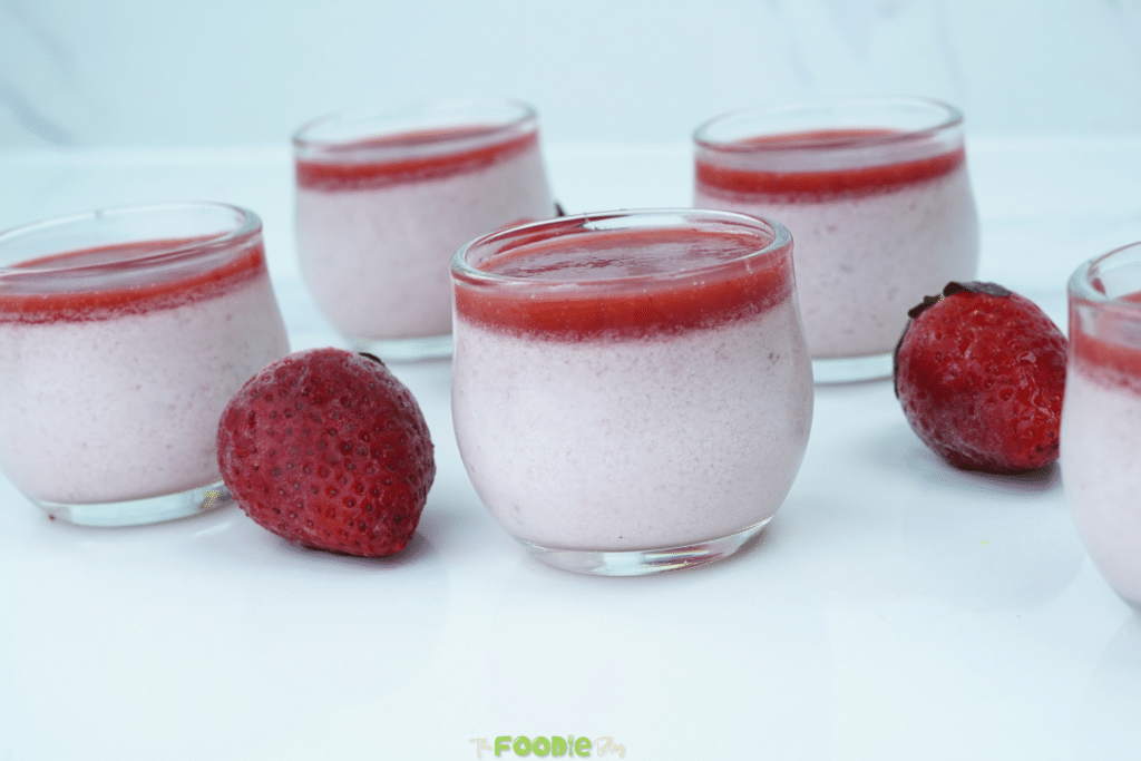 Strawberry panna cotta in small glass cups with a strawberry topping and fresh strawberries on the side