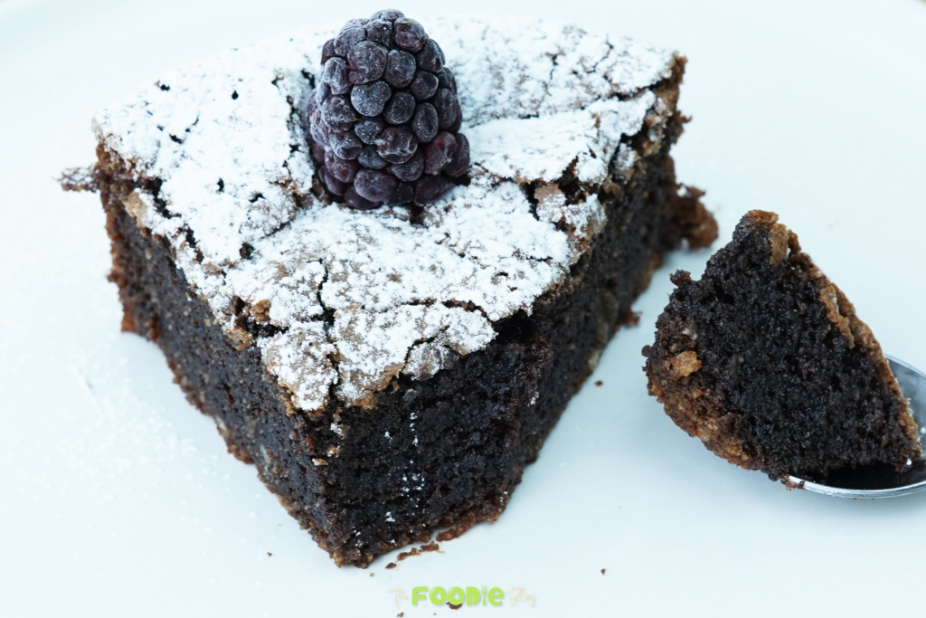 Close-up of a torta caprese slice dusted with powdered sugar and topped with a blackberry on a white plate