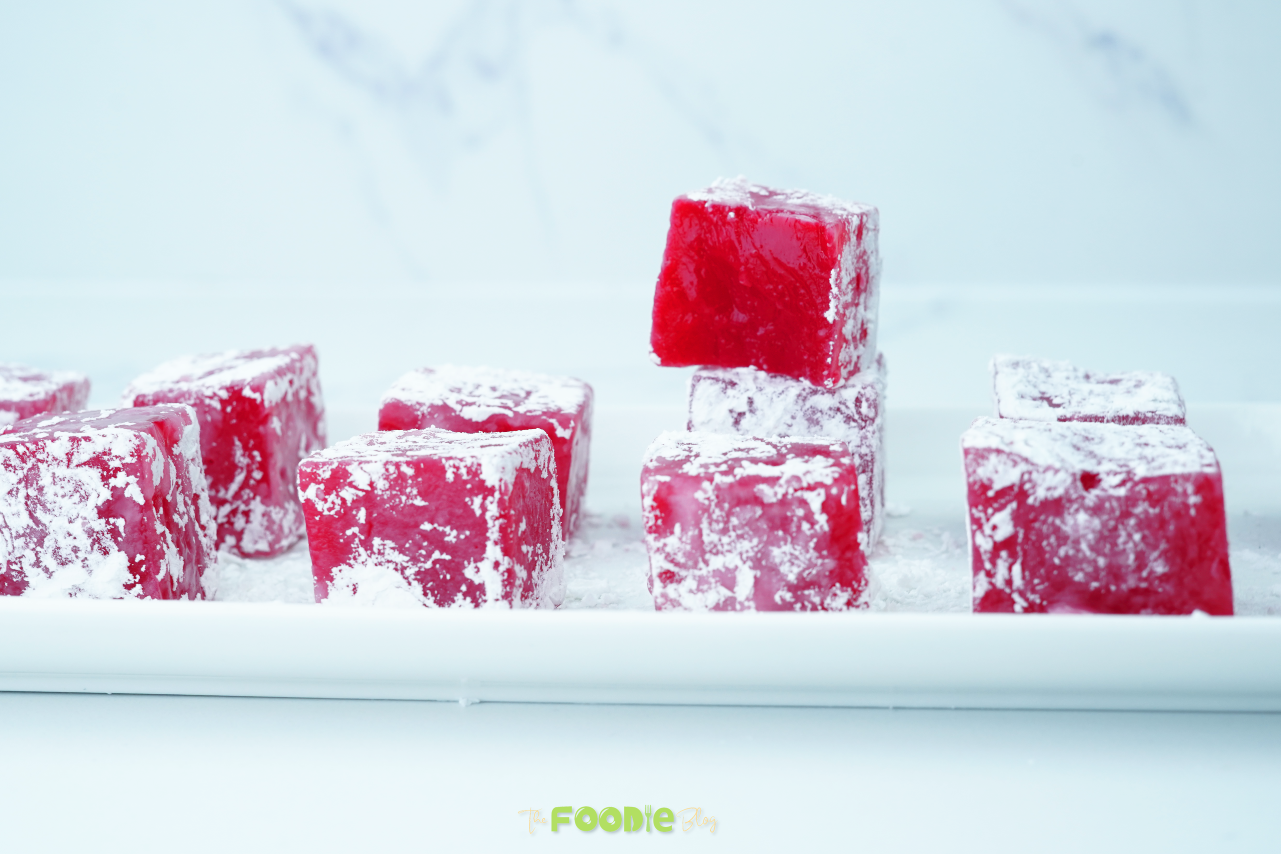 A tray of Turkish Delight cubes coated in powdered sugar with one cube stacked on top