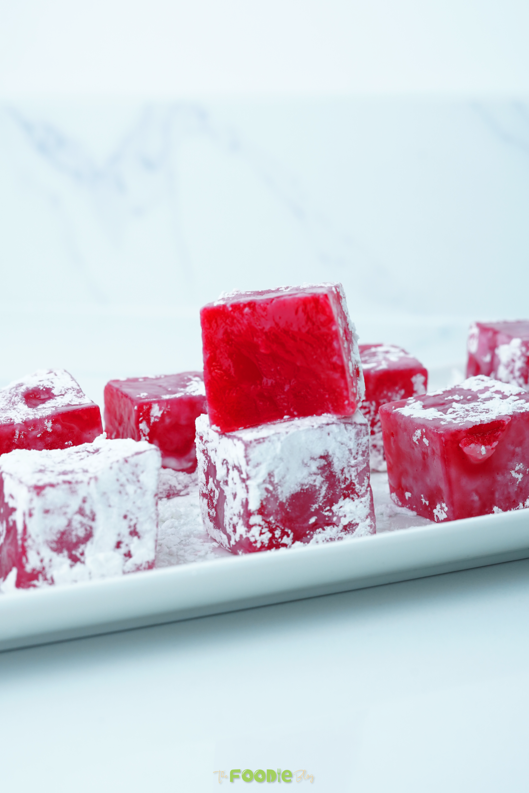 Close-up of rose Turkish Delight cubes with powdered sugar on a white tray