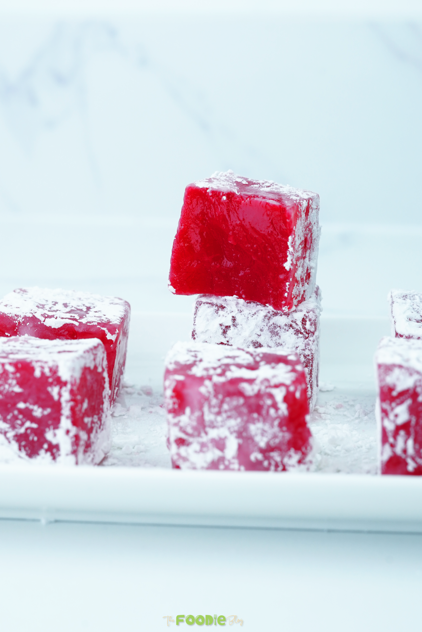 Red Turkish Delight cubes dusted with powdered sugar on a white tray