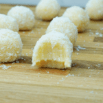 Close-up of a bitten coconut-coated white chocolate truffle with other truffles blurred in the background