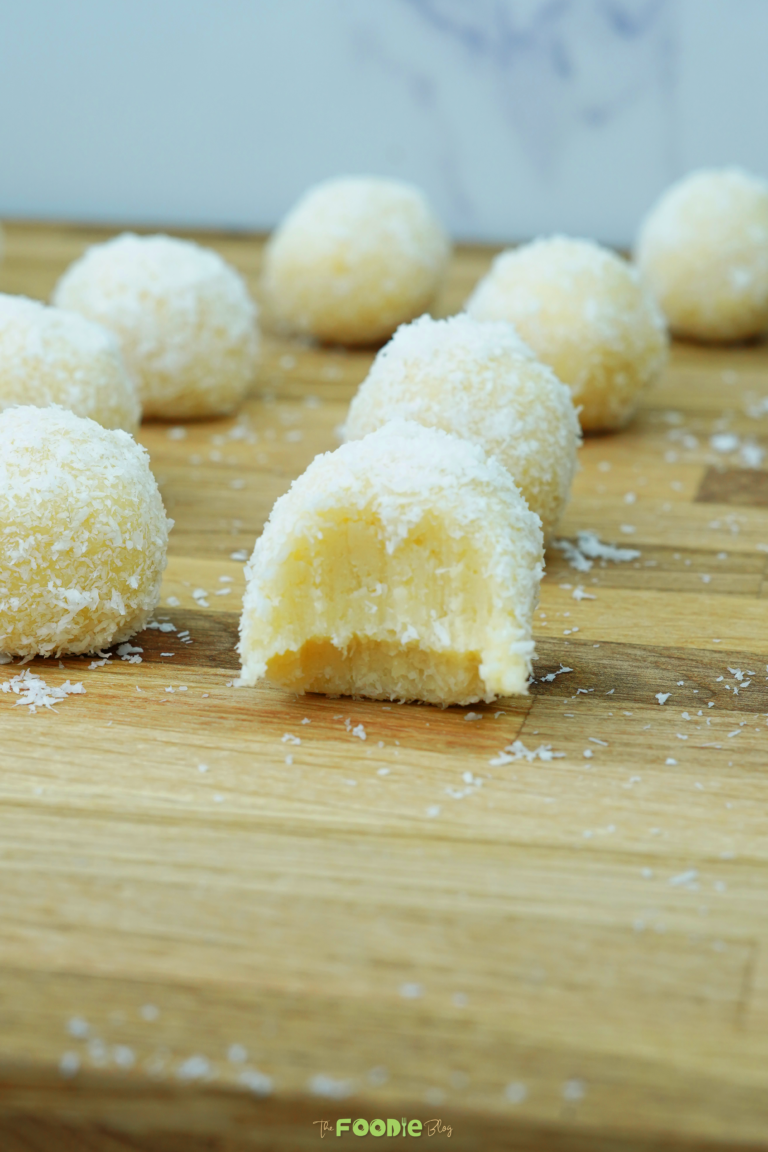 Close-up of a bitten coconut-coated white chocolate truffle with other truffles blurred in the background