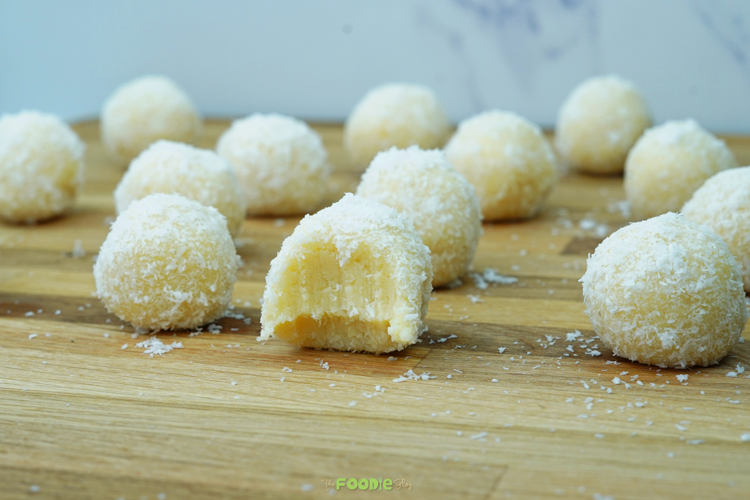 Coconut-coated white chocolate truffles arranged on a wooden board with coconut flakes scattered around