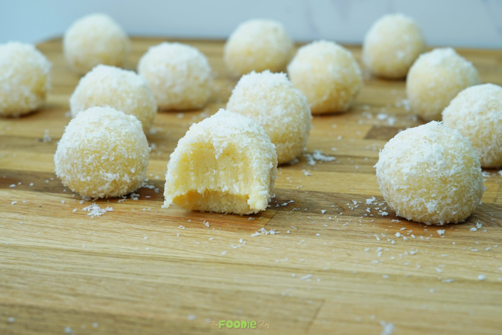 Coconut-coated white chocolate truffles on a wooden board with one truffle bitten to show the creamy center