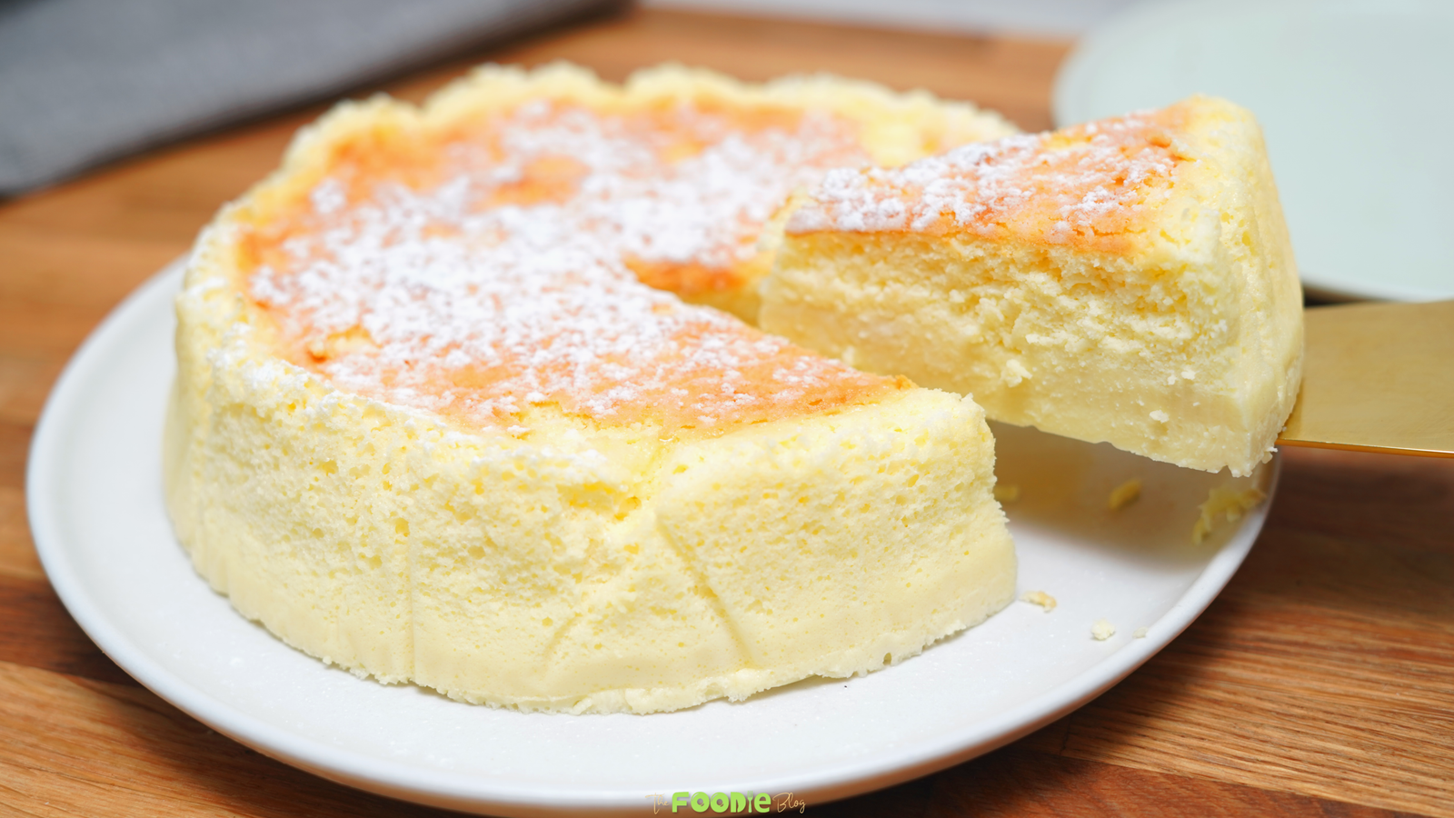 Whole Japanese cheesecake dusted with powdered sugar on a white plate with a slice being lifted