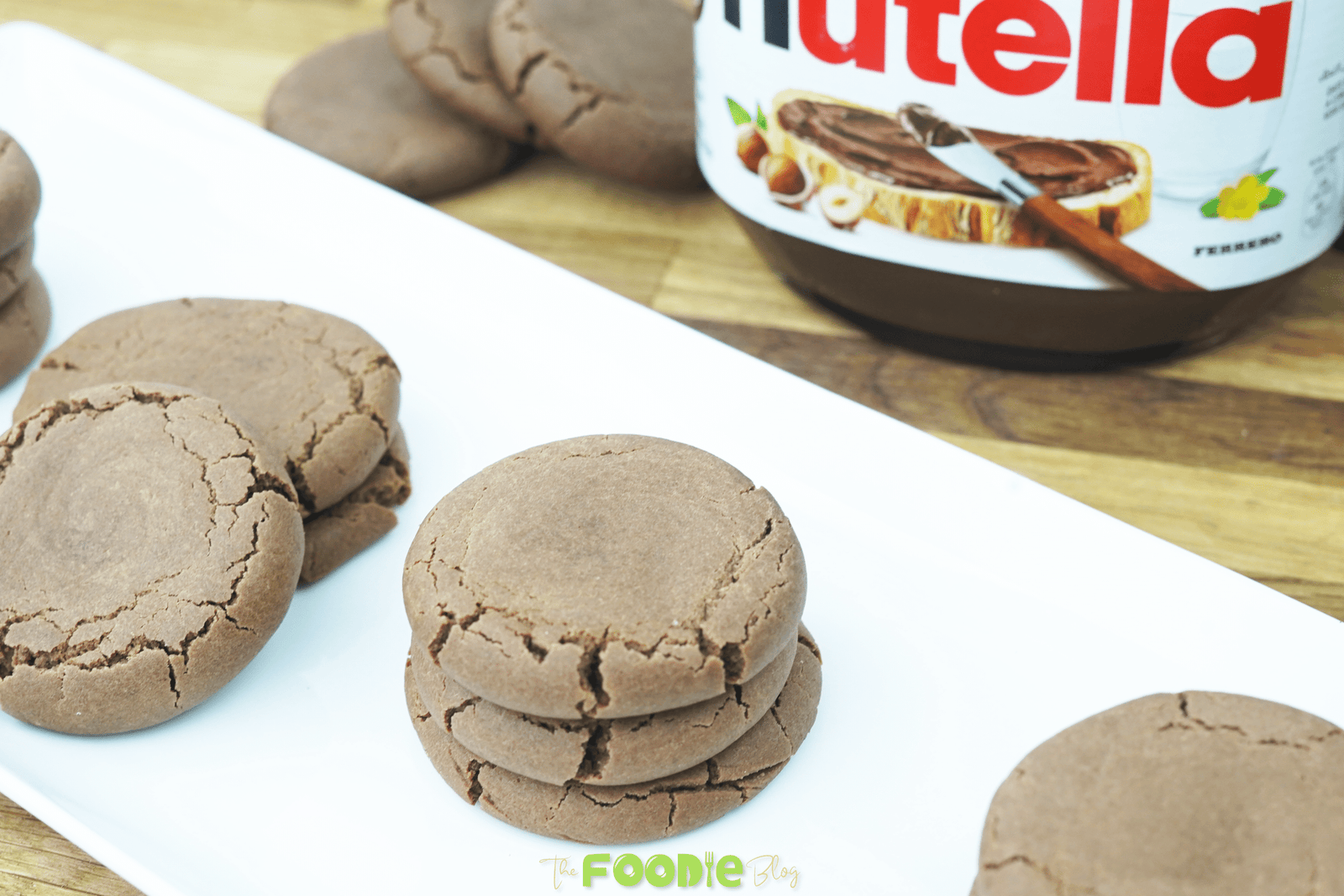 Soft Nutella cookies stacked on a white plate with a jar of Nutella in the background