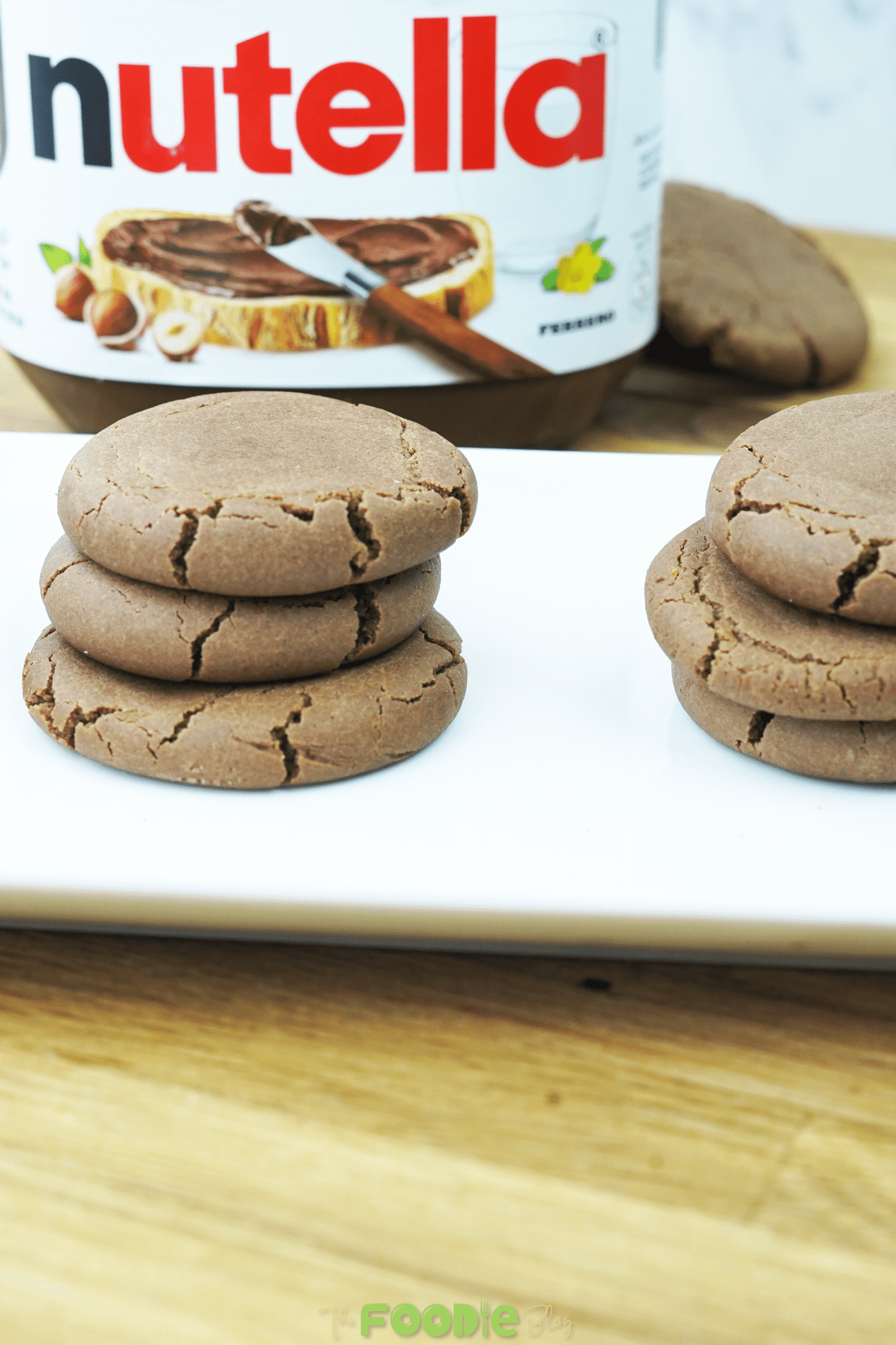 Nutella cookies stacked on a serving plate with the Nutella jar in the background