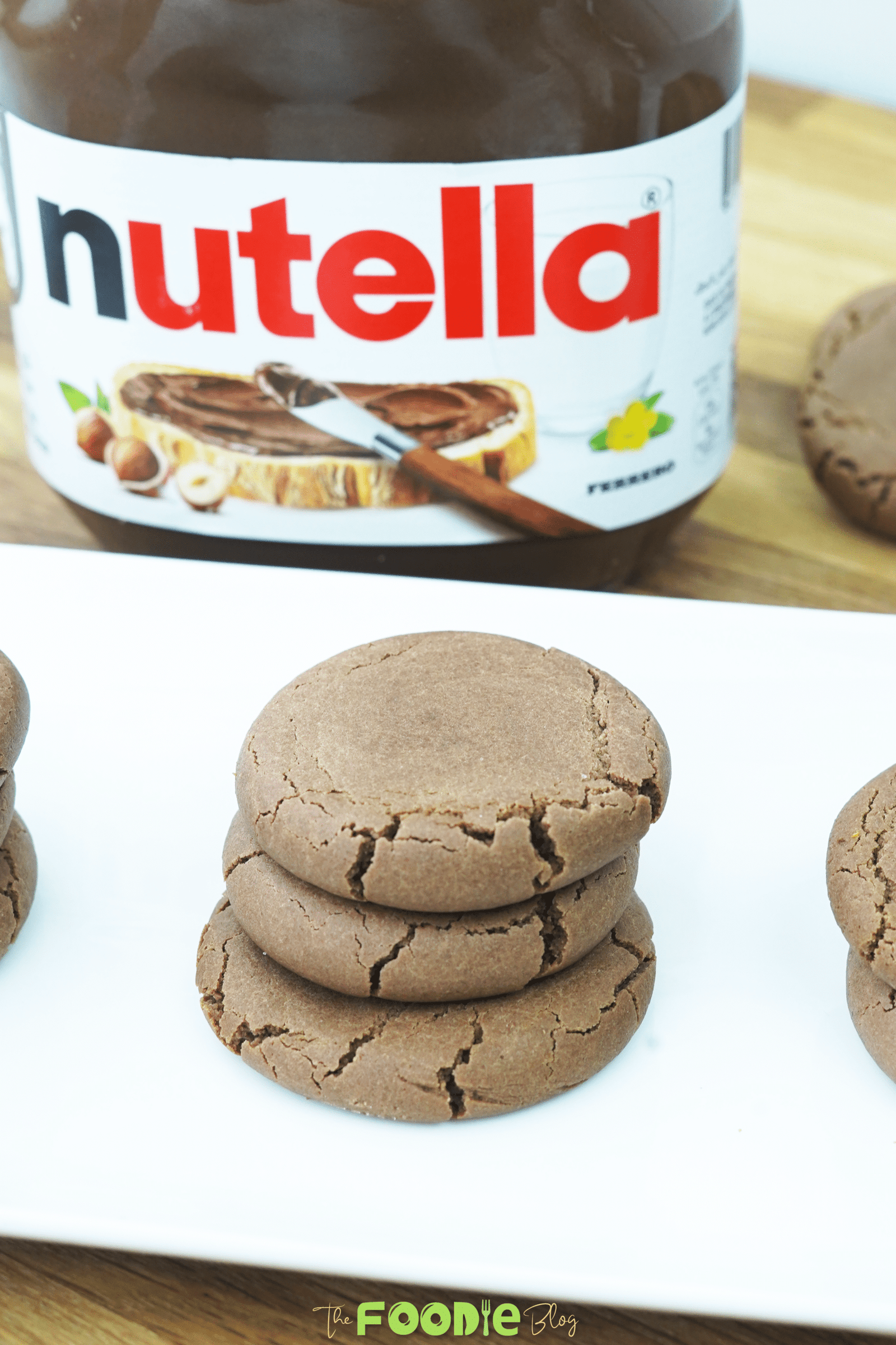 Three Nutella cookies stacked on a white plate with cracked tops