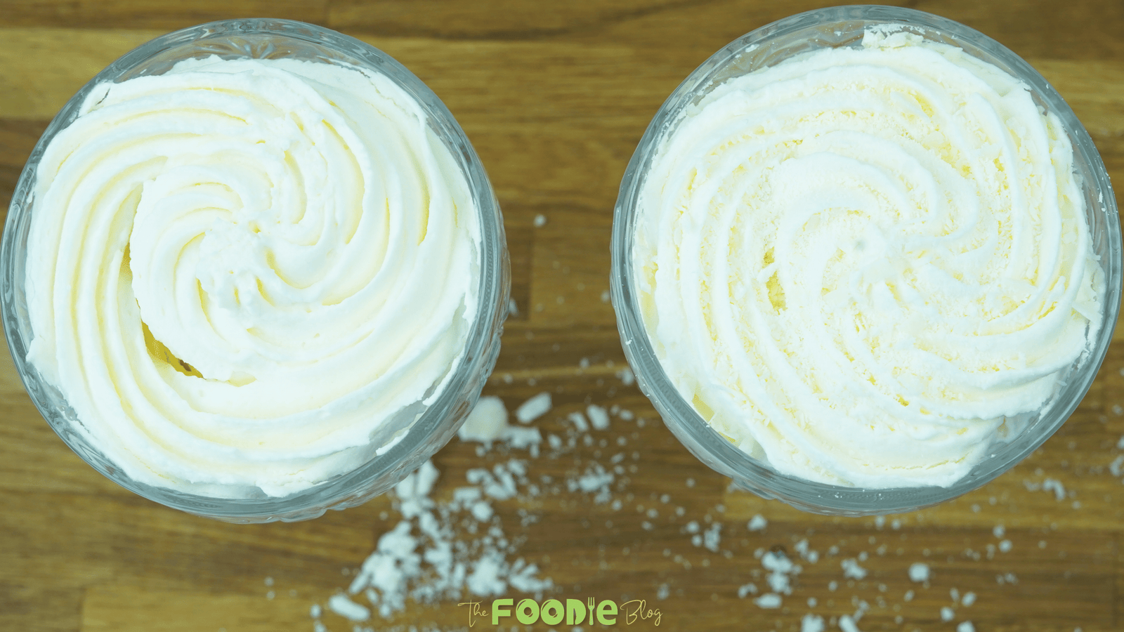 Two glasses of white chocolate mousse topped with piped swirls and white chocolate shavings