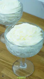 A glass of white chocolate mousse with a piped top served on a wooden surface