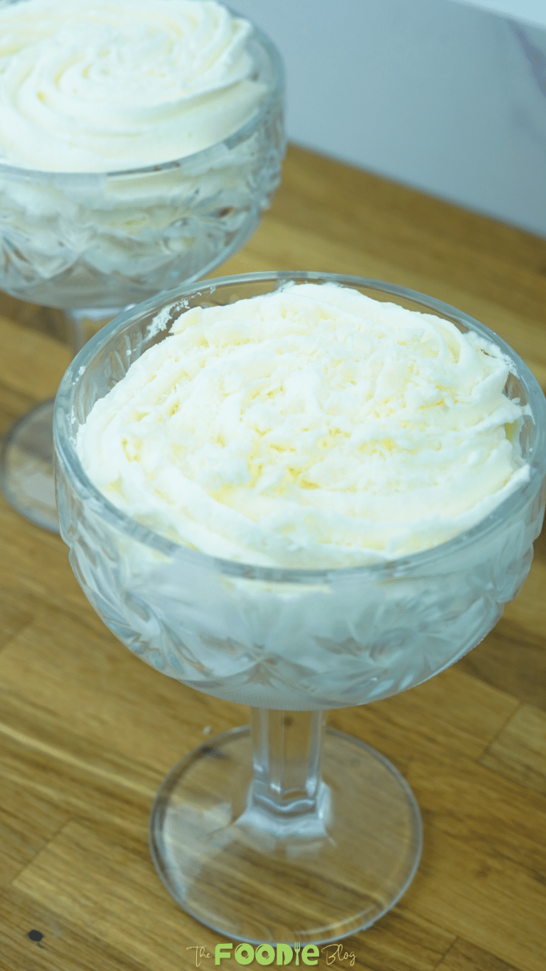 A glass of white chocolate mousse with a piped top served on a wooden surface