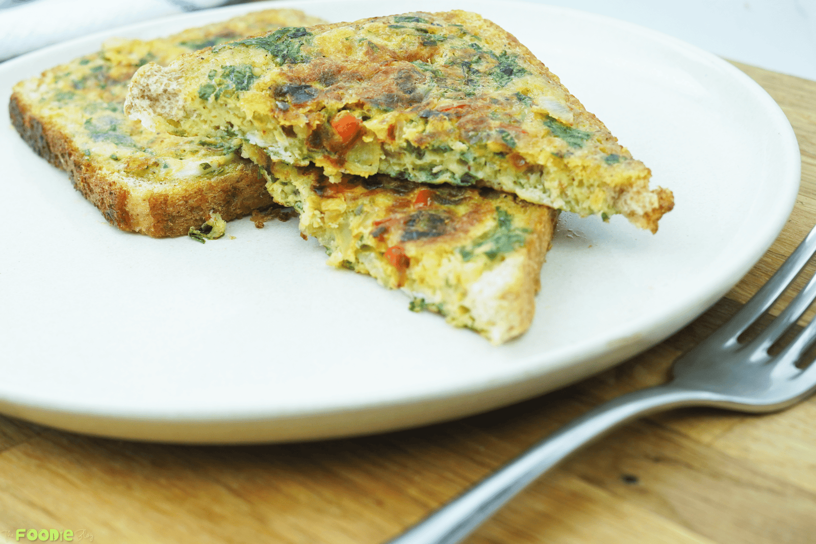 Close-up of bread omelette slices on a white plate with visible onion, herbs, and diced bell pepper inside