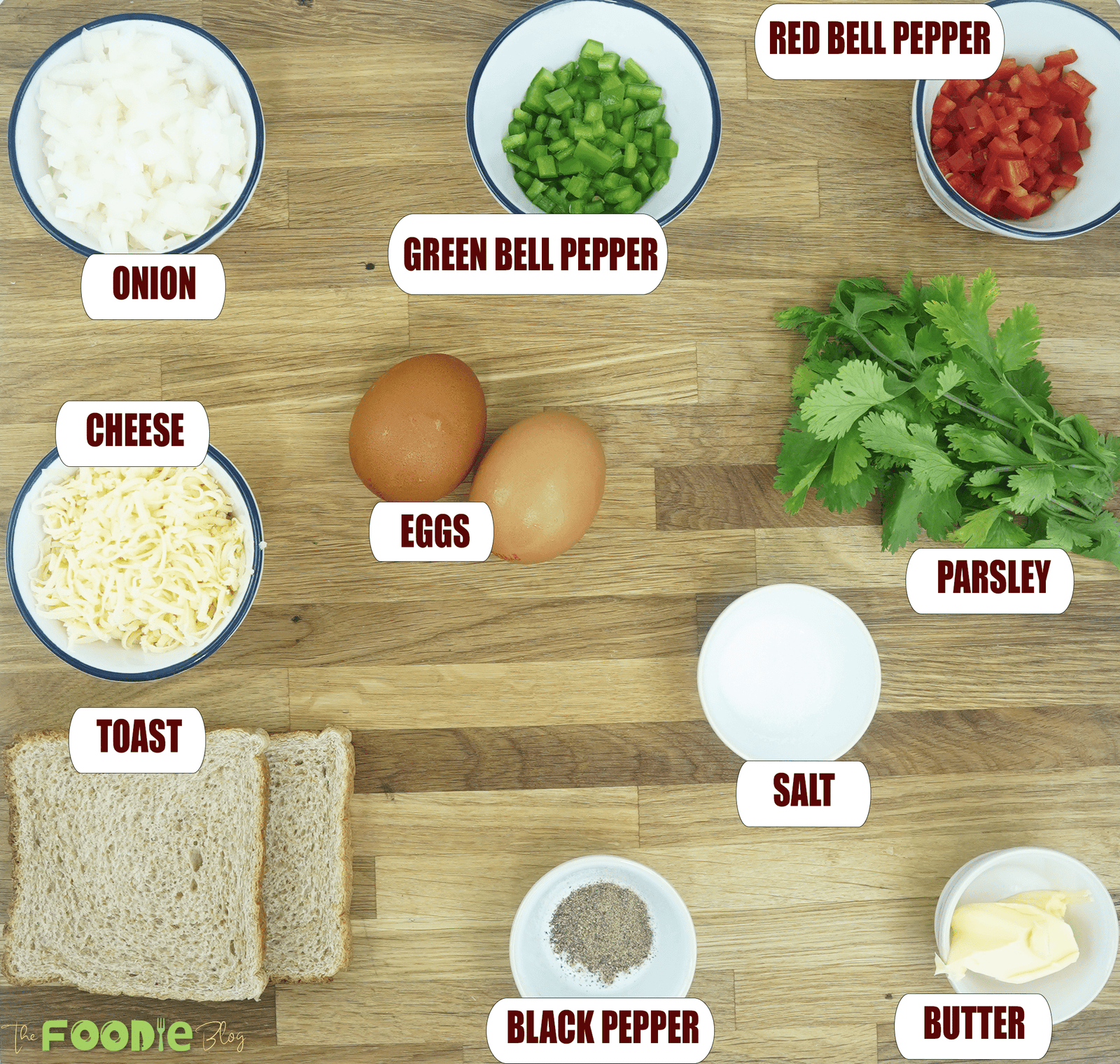 Overhead view of bread omelette ingredients including eggs, shredded cheese, onion, bell peppers, parsley, bread, butter, salt, and black pepper