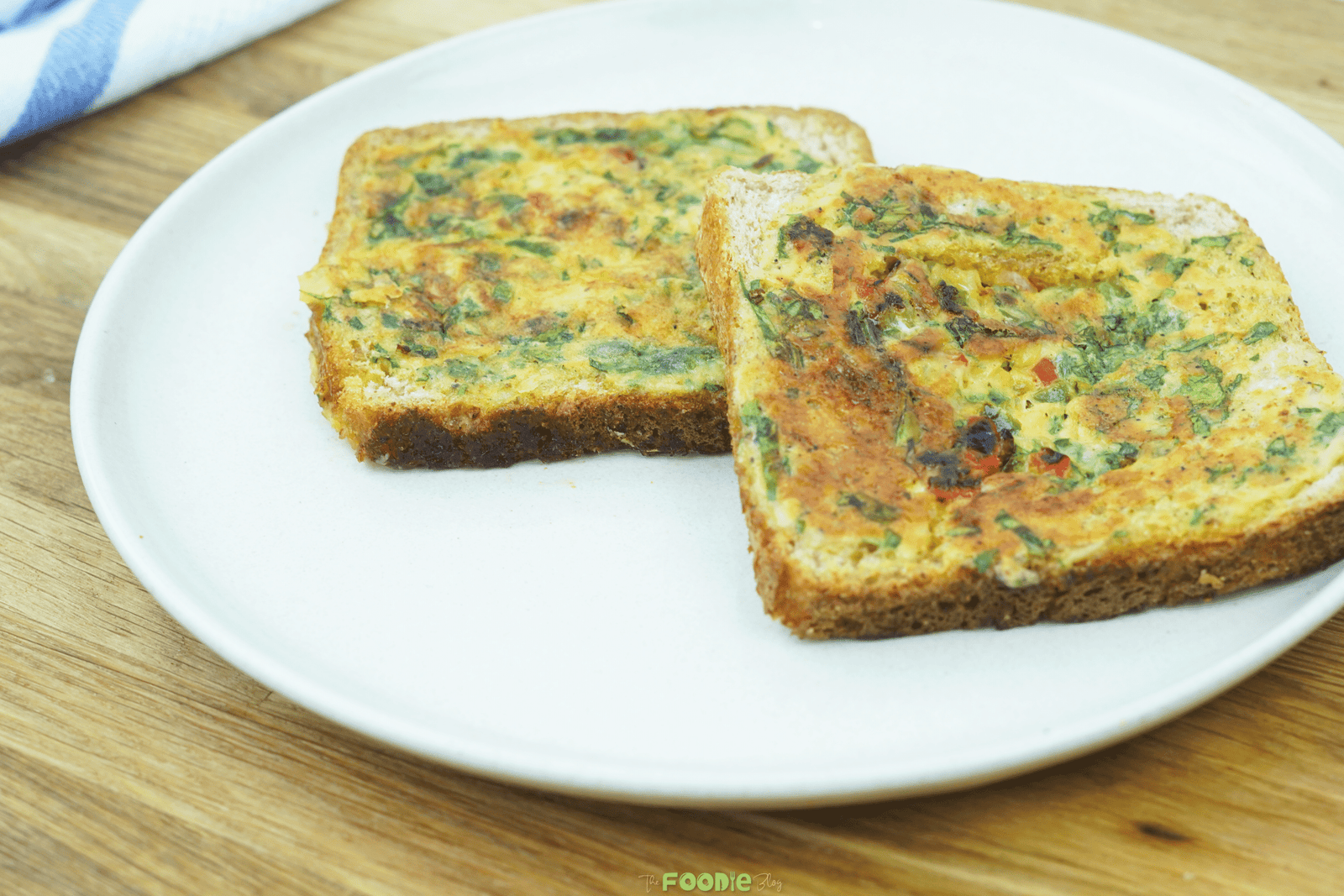 Two whole slices of bread omelette on a plate with golden tops and visible herbs and peppers