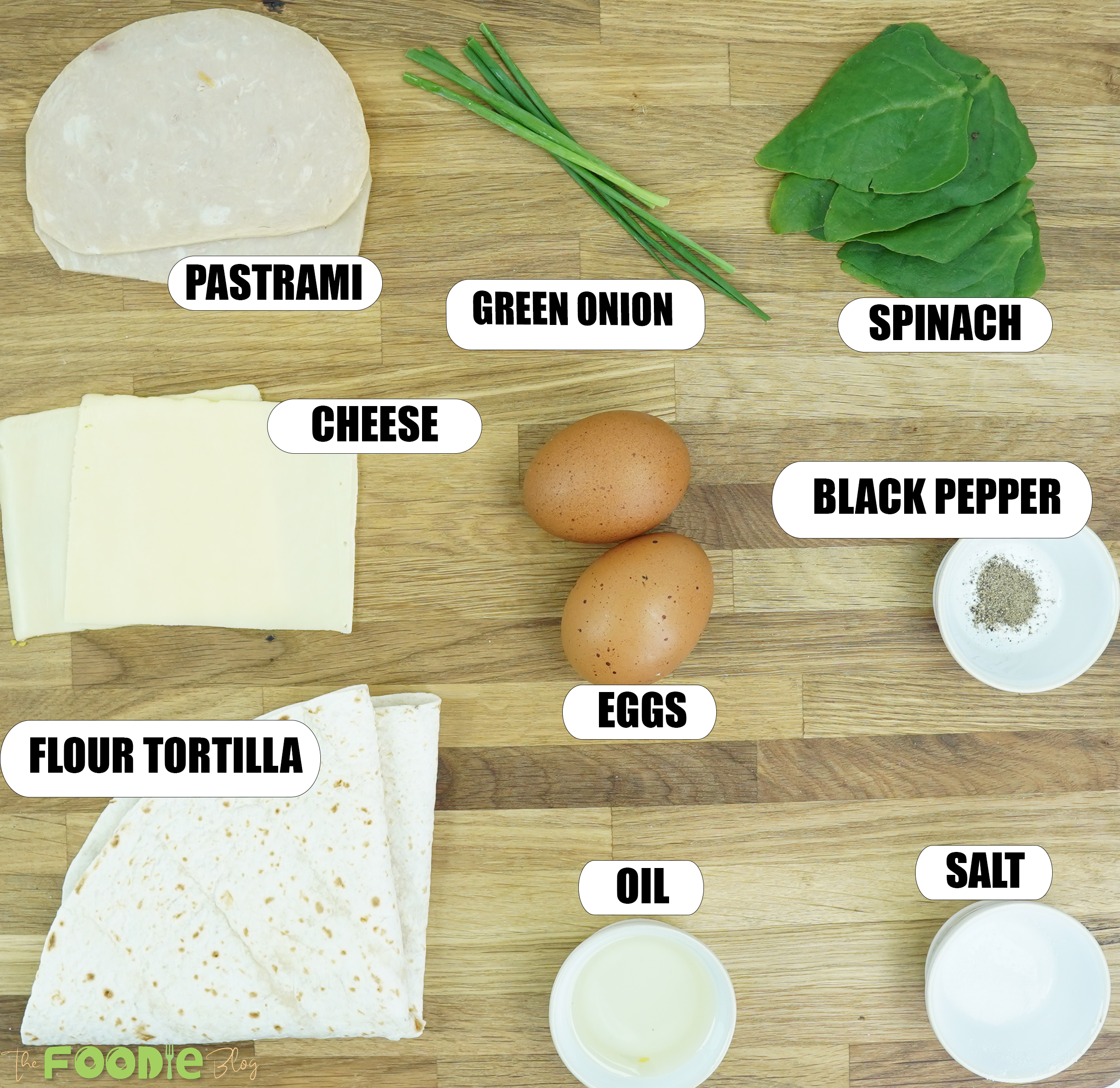 ingredients for breakfast borito arranged on a wooden surface including eggs, tortilla, cheese, pastrami, spinach, green onion, salt, pepper, and oil