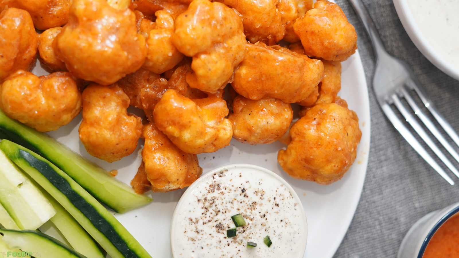 Close-up of buffalo cauliflower wings on a plate with celery sticks and a small bowl of ranch dressing.