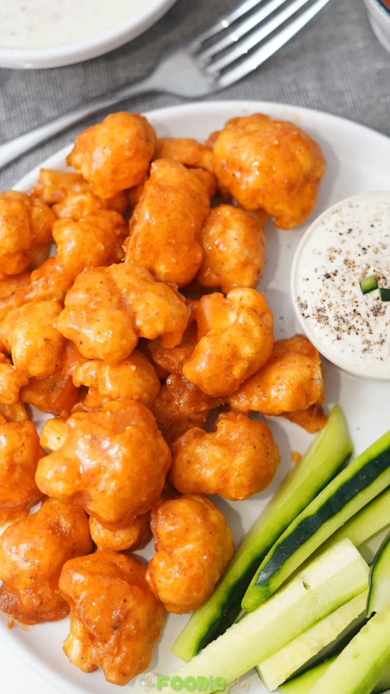 Buffalo cauliflower wings served on a white plate with cashew ranch dressing and celery sticks.