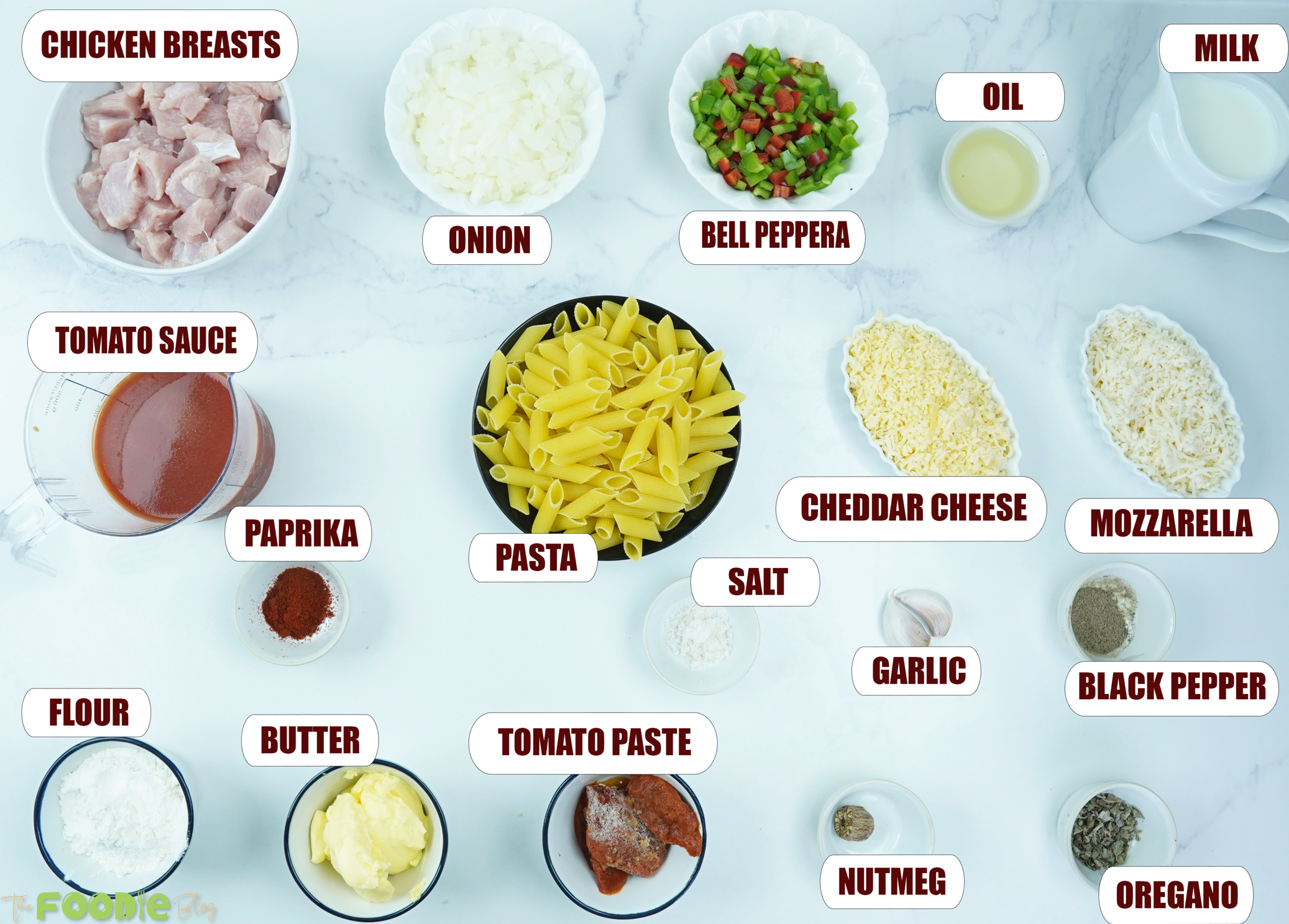 ingredients for chicken pasta bake arranged on a white surface including chicken, pasta, cheeses, milk, onion, and peppers