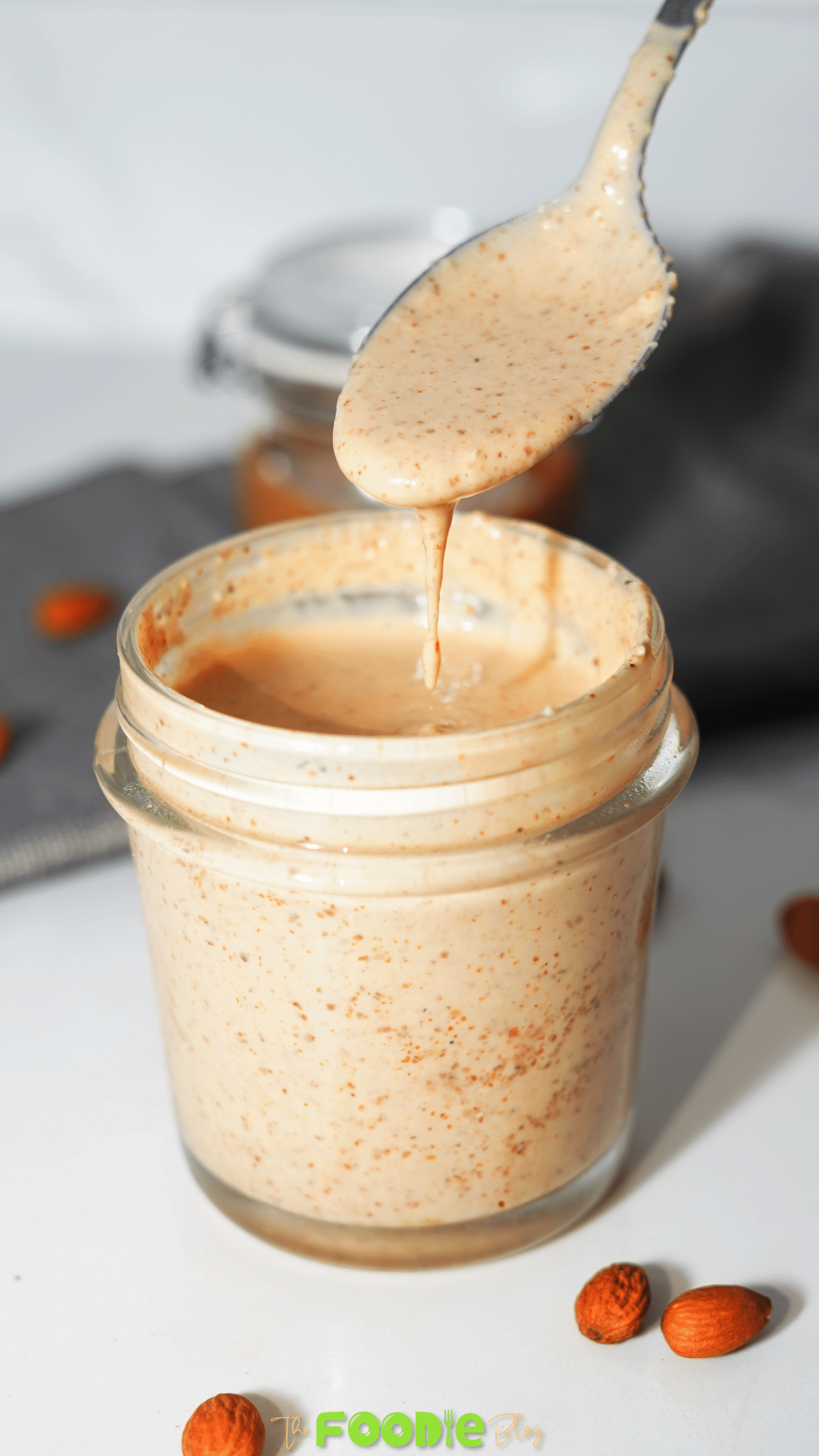 Spoon dripping creamy chili almond dressing back into a small glass jar.