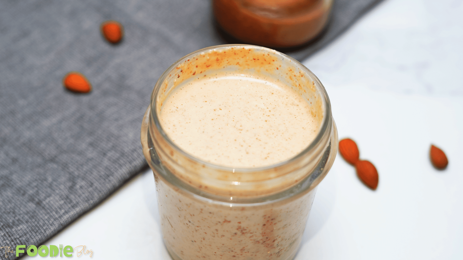 Top view of a small glass jar filled with creamy chili almond dressing on a light surface.
