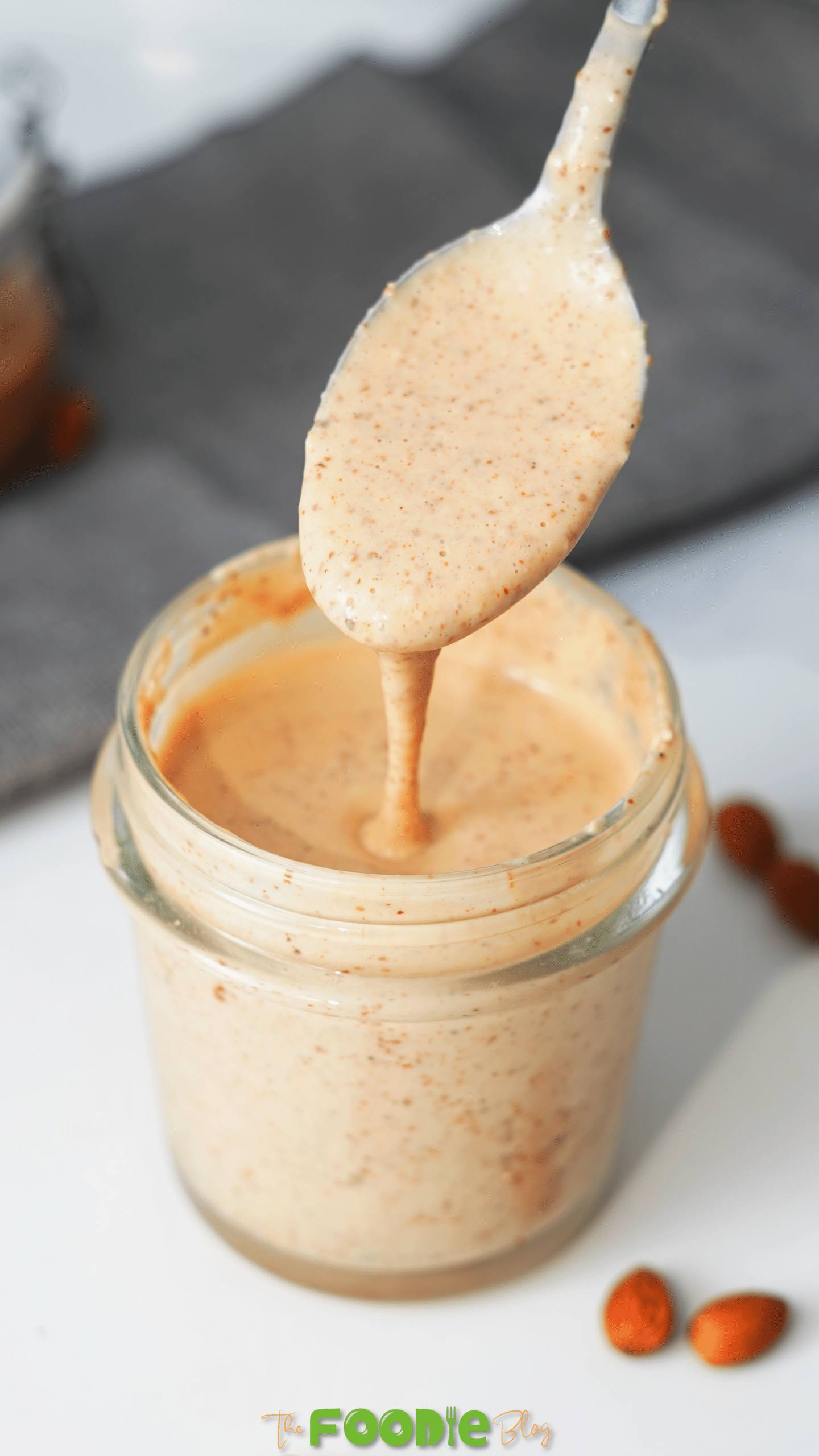 Close-up of a spoon holding creamy chili almond dressing above a jar.