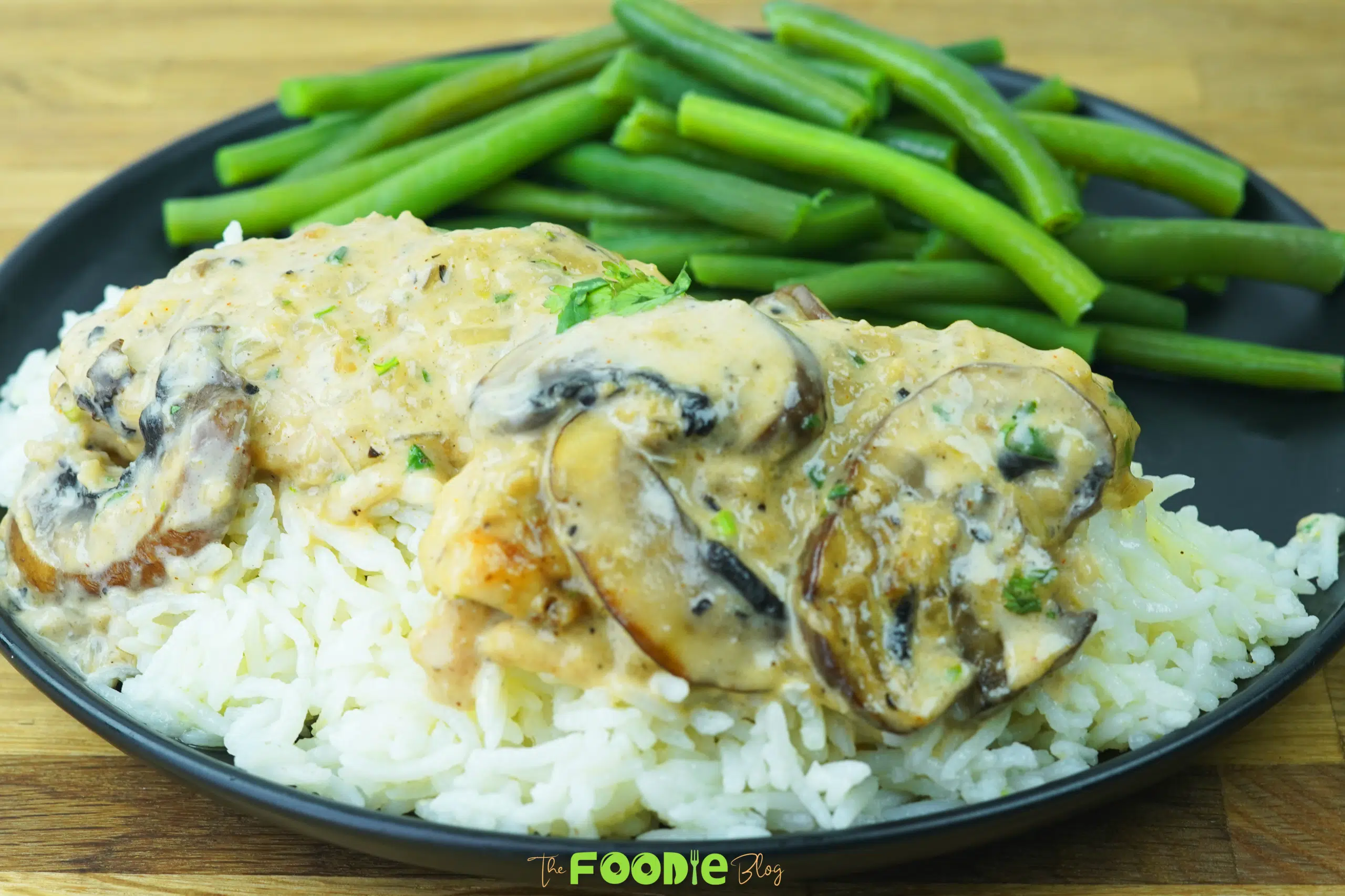 Creamy mushroom chicken served over white rice with green beans on a black plate