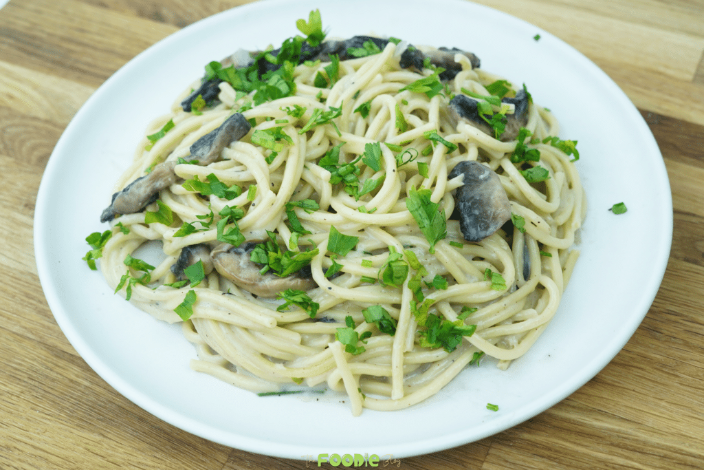 Creamy mushroom pasta served on a white plate and topped with fresh chopped parsley