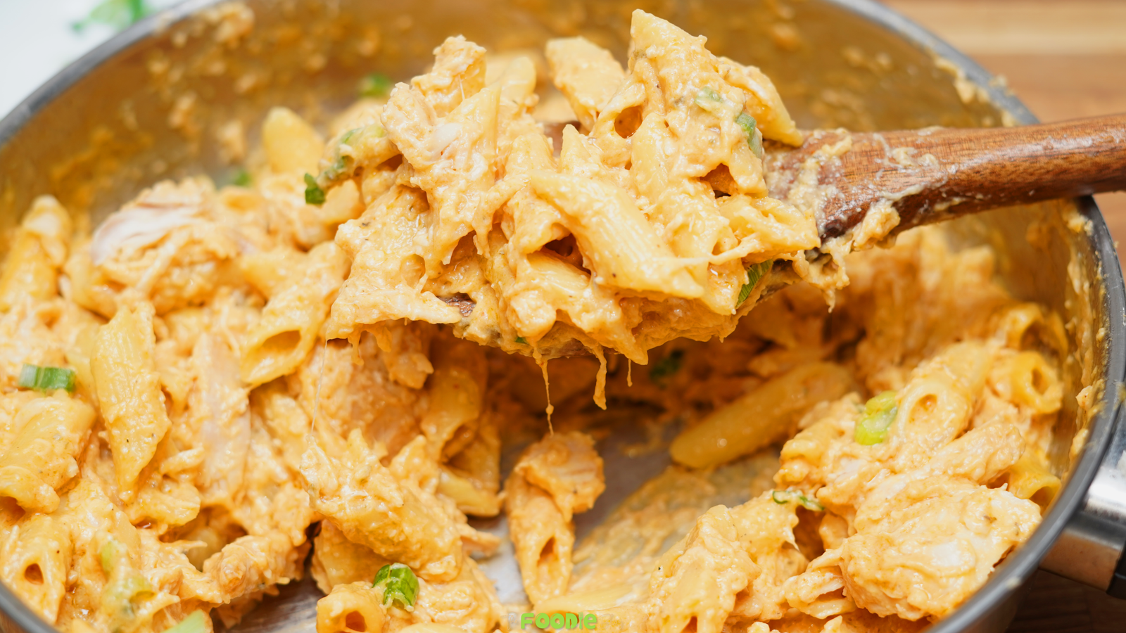 Close-up of creamy Buffalo chicken pasta in a pot with penne, shredded chicken, melted cheese, and green onions.