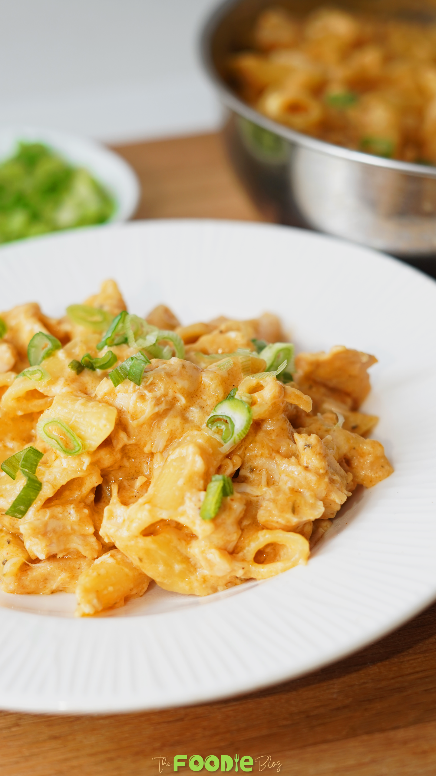 Creamy Buffalo chicken pasta served on a white plate with chopped green onions on top and a pot of pasta in the background.