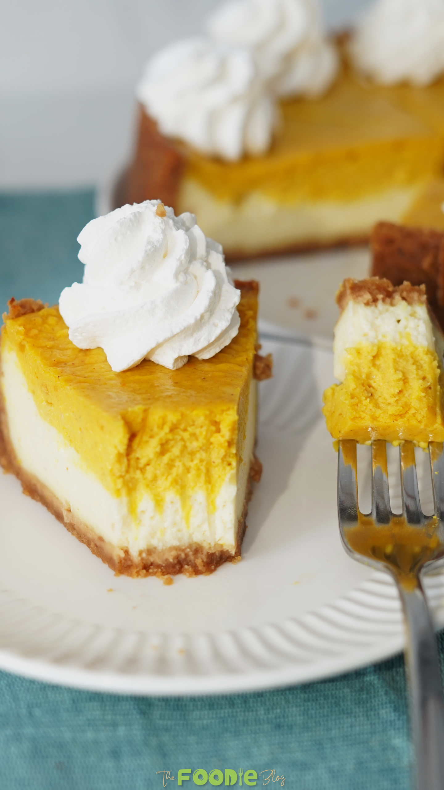 A close-up of pumpkin pie cheesecake with whipped cream and a fork holding a bite of creamy pumpkin cheesecake.