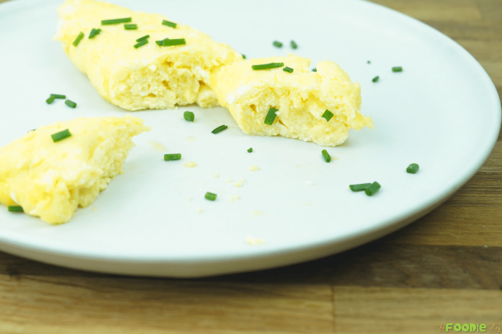 Cut French omelette on a plate showing the soft interior with chopped chives scattered around