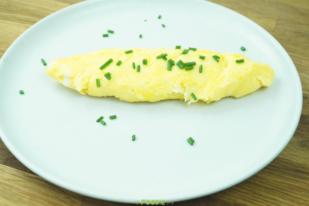Whole French omelette on a plate with chopped chives scattered over the top