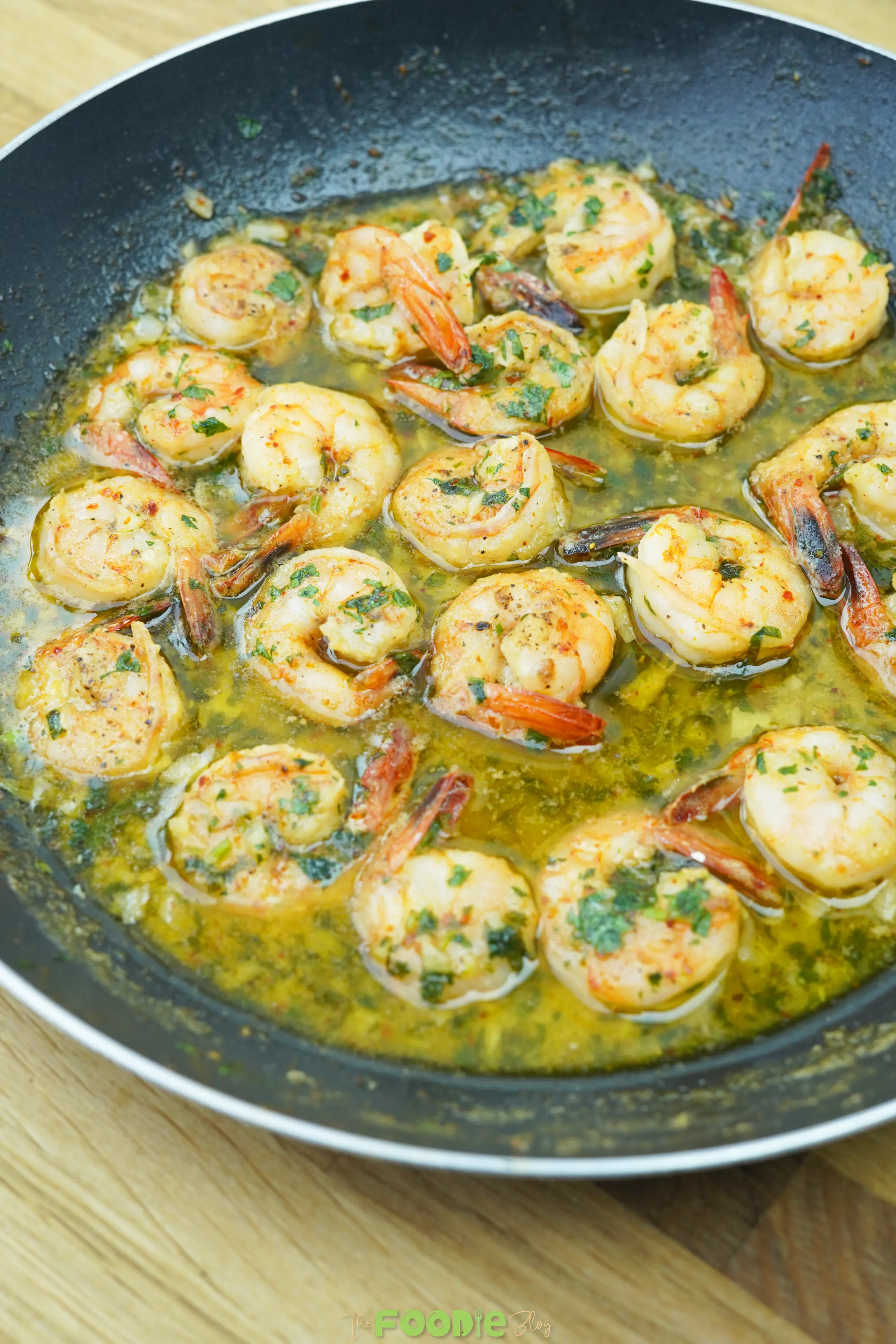 Close-up of shrimp in garlic butter and white wine sauce with chopped parsley in a skillet