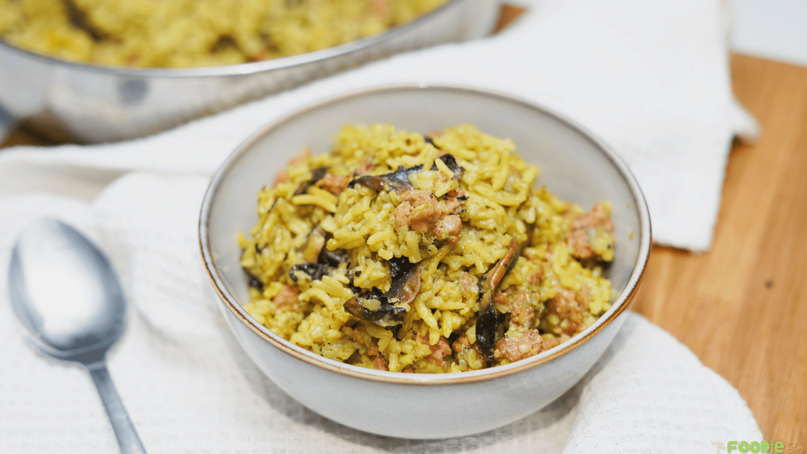 Bowl of ground turkey casserole with rice and mushrooms served on a white cloth with the skillet in the background